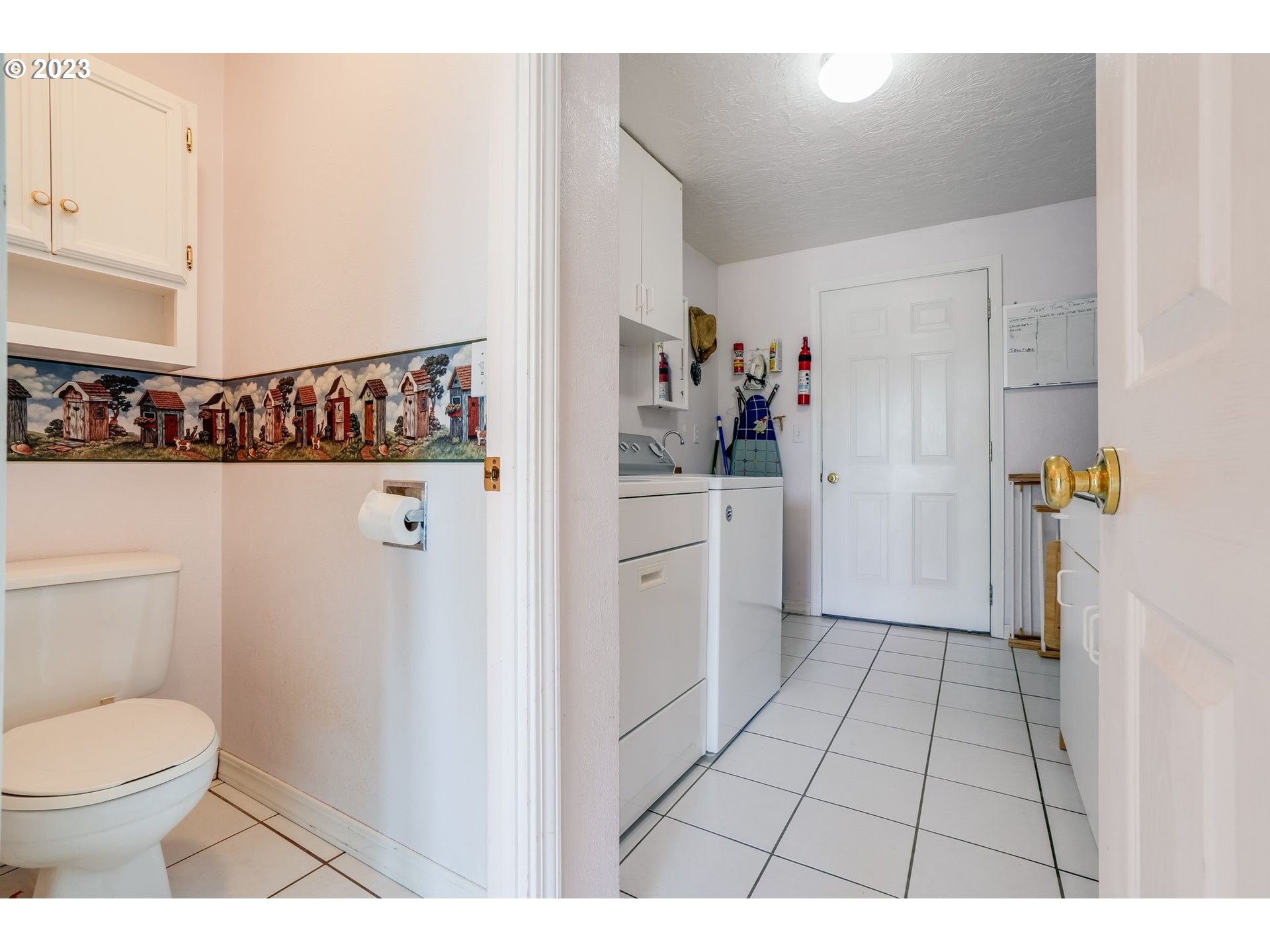 Laundry room with washer and dryer, viewed through a bathroom with a decorative wall border.