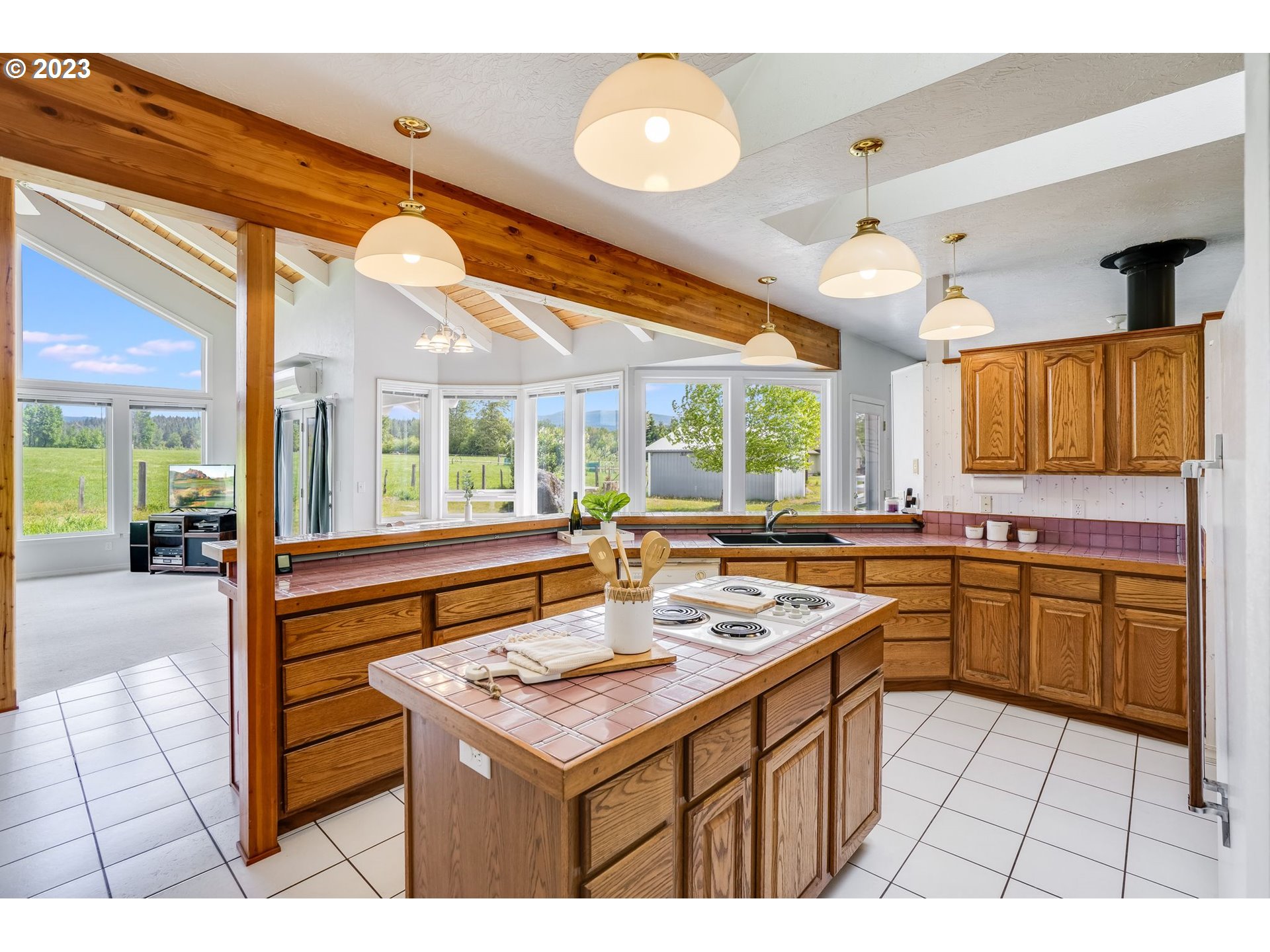 Kitchen with oak cabinets, pink tile counters, and large windows overlooking green fields.