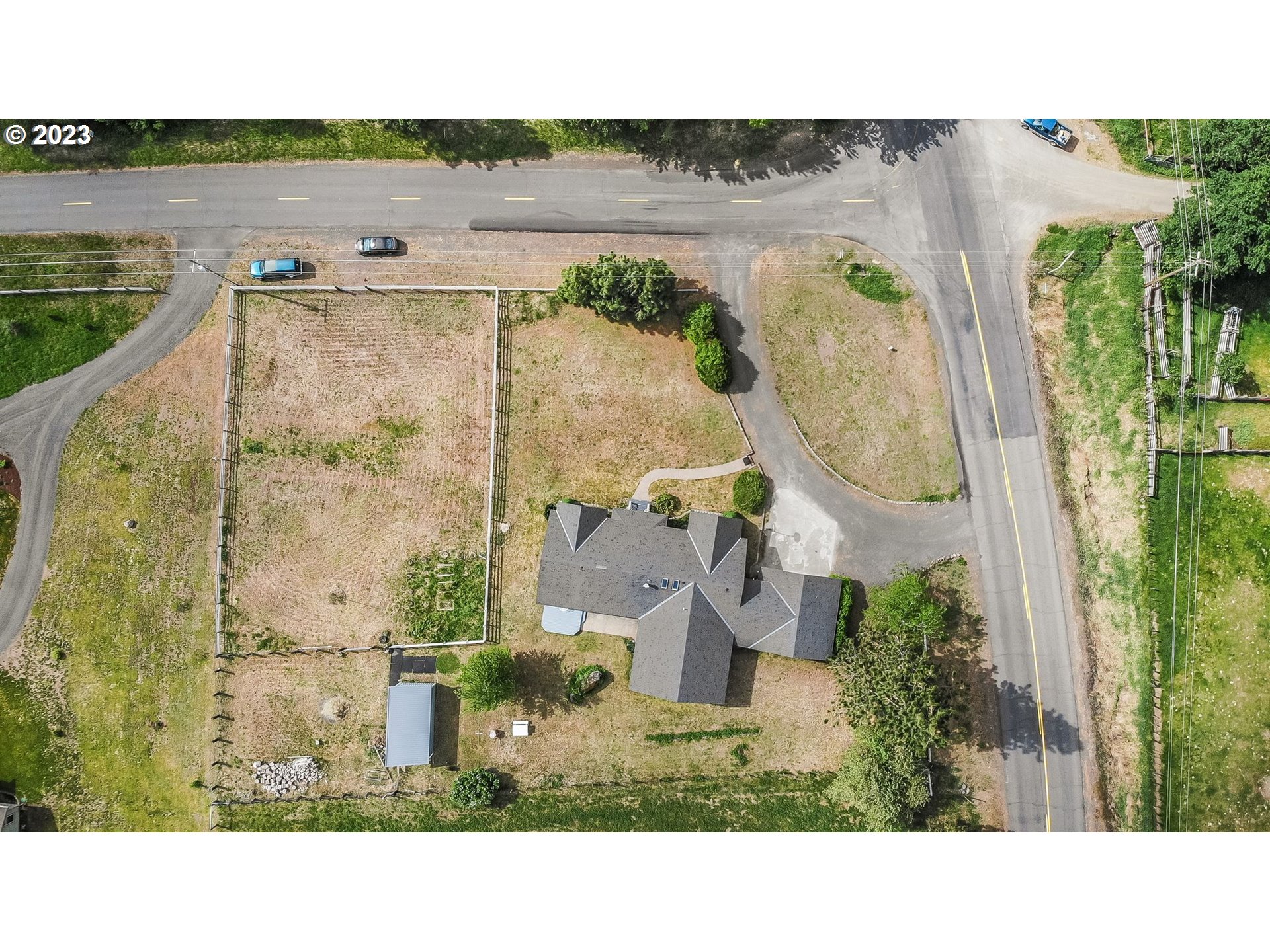Aerial view of a house on a corner lot with a large fenced yard and detached shed.