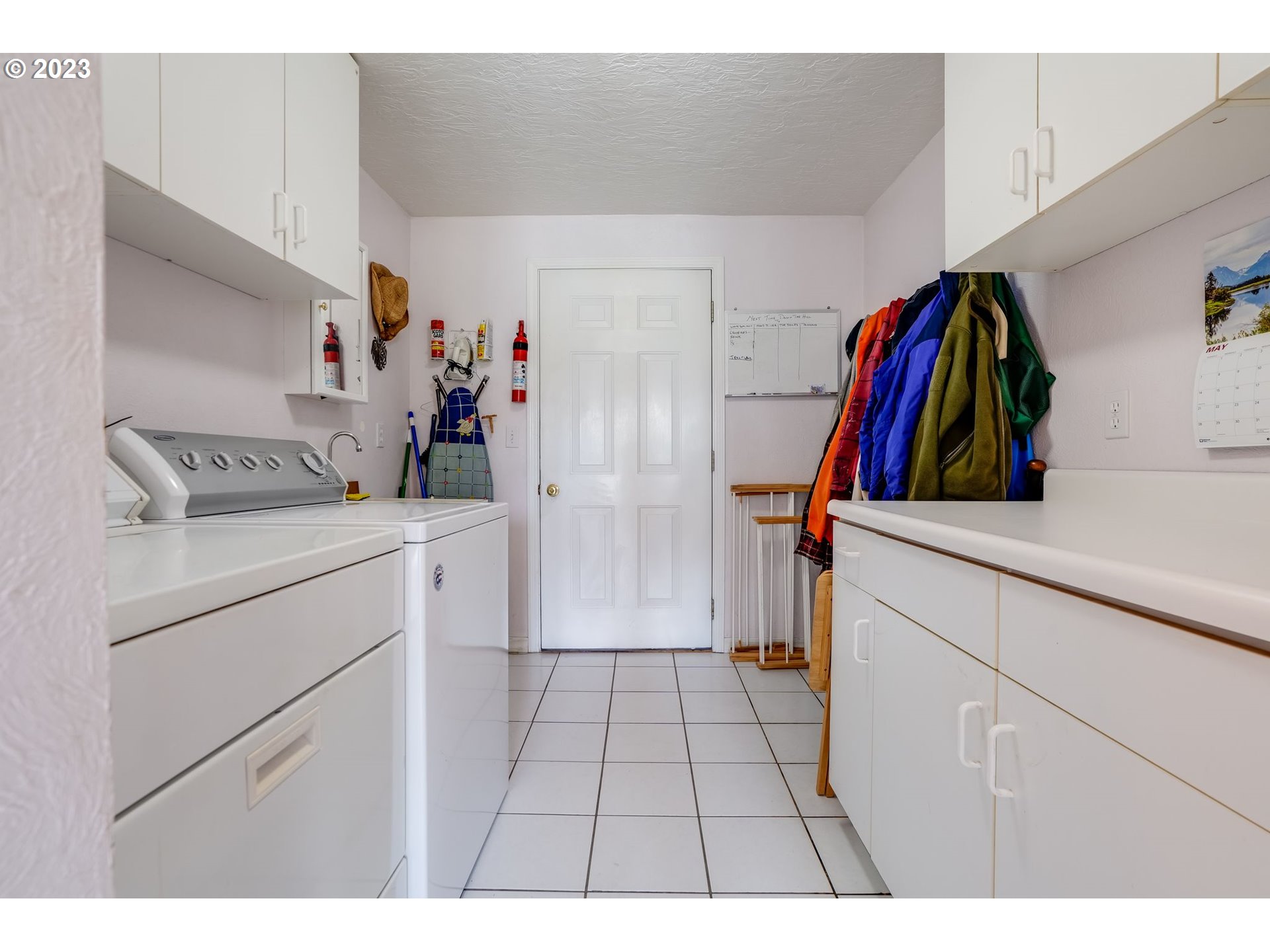 Laundry room with washer and dryer, white cabinets, tiled floor, and coats hanging beside the back door.
