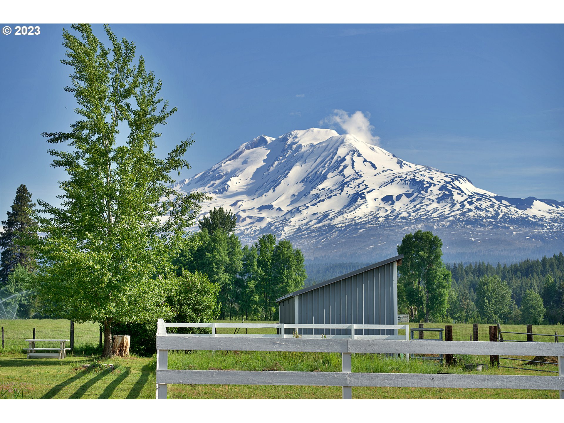 Rural property with a fenced paddock and metal outbuilding beneath snow-covered Mount Adams.