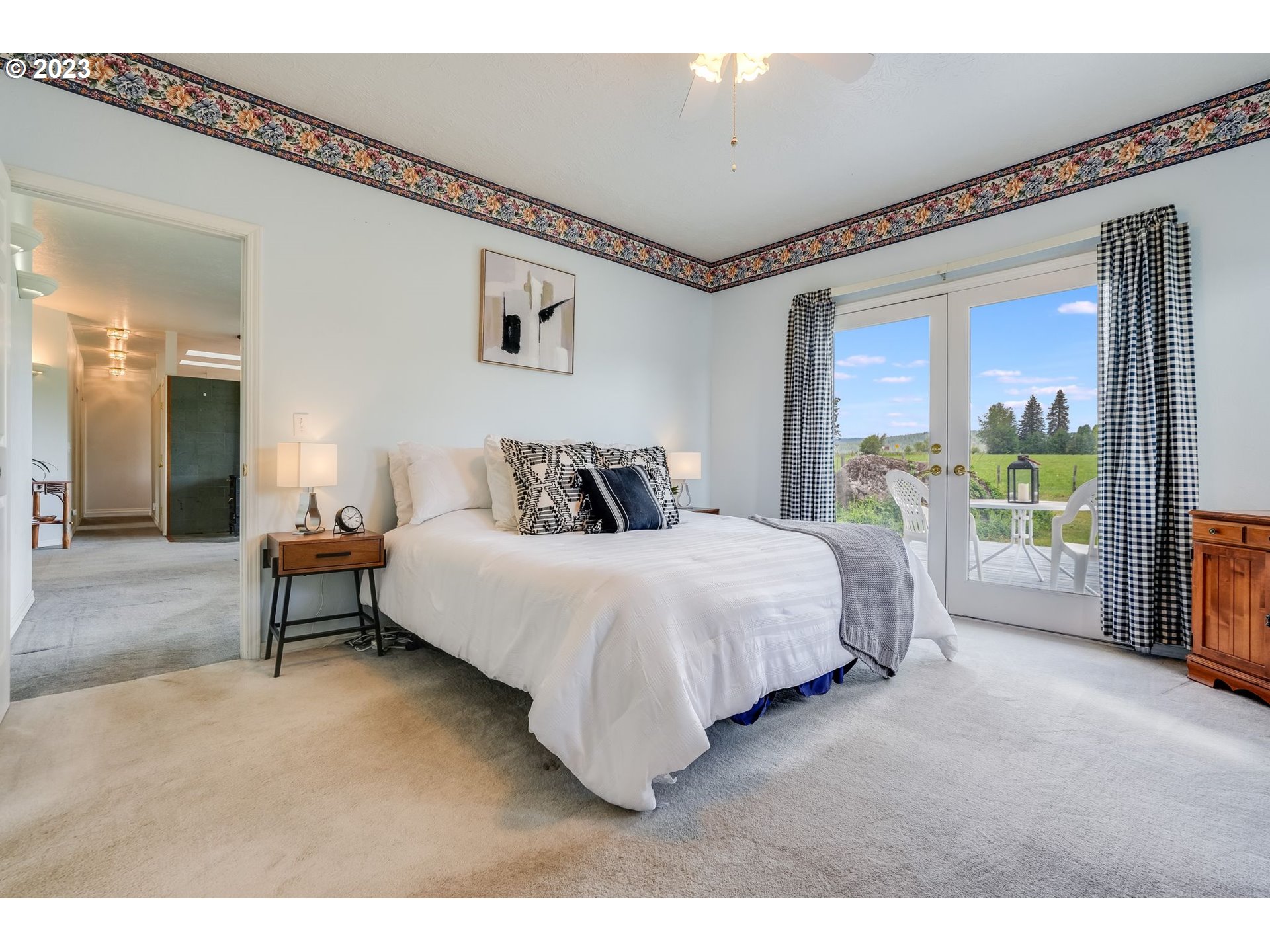 Bedroom with a white bed and French doors overlooking a green lawn.