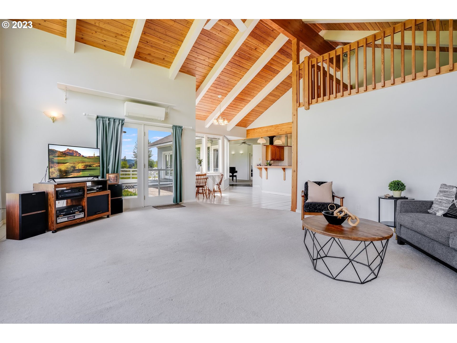 Living room with a vaulted wood ceiling, loft railing, and open dining area.