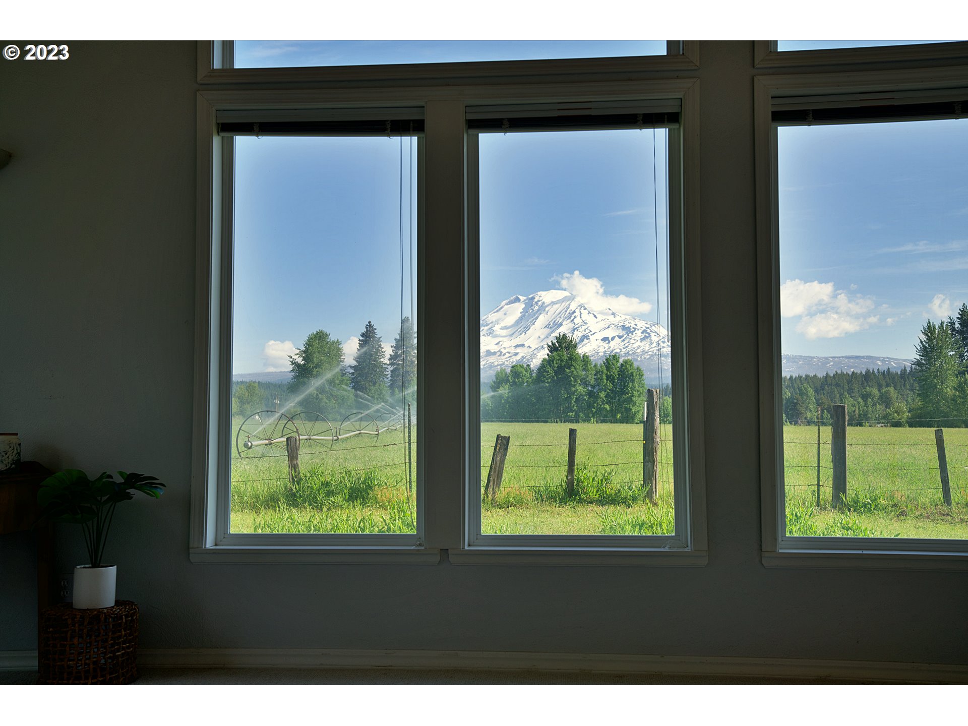 Snow-covered Mount Adams framed by living-room windows above a green fenced field.