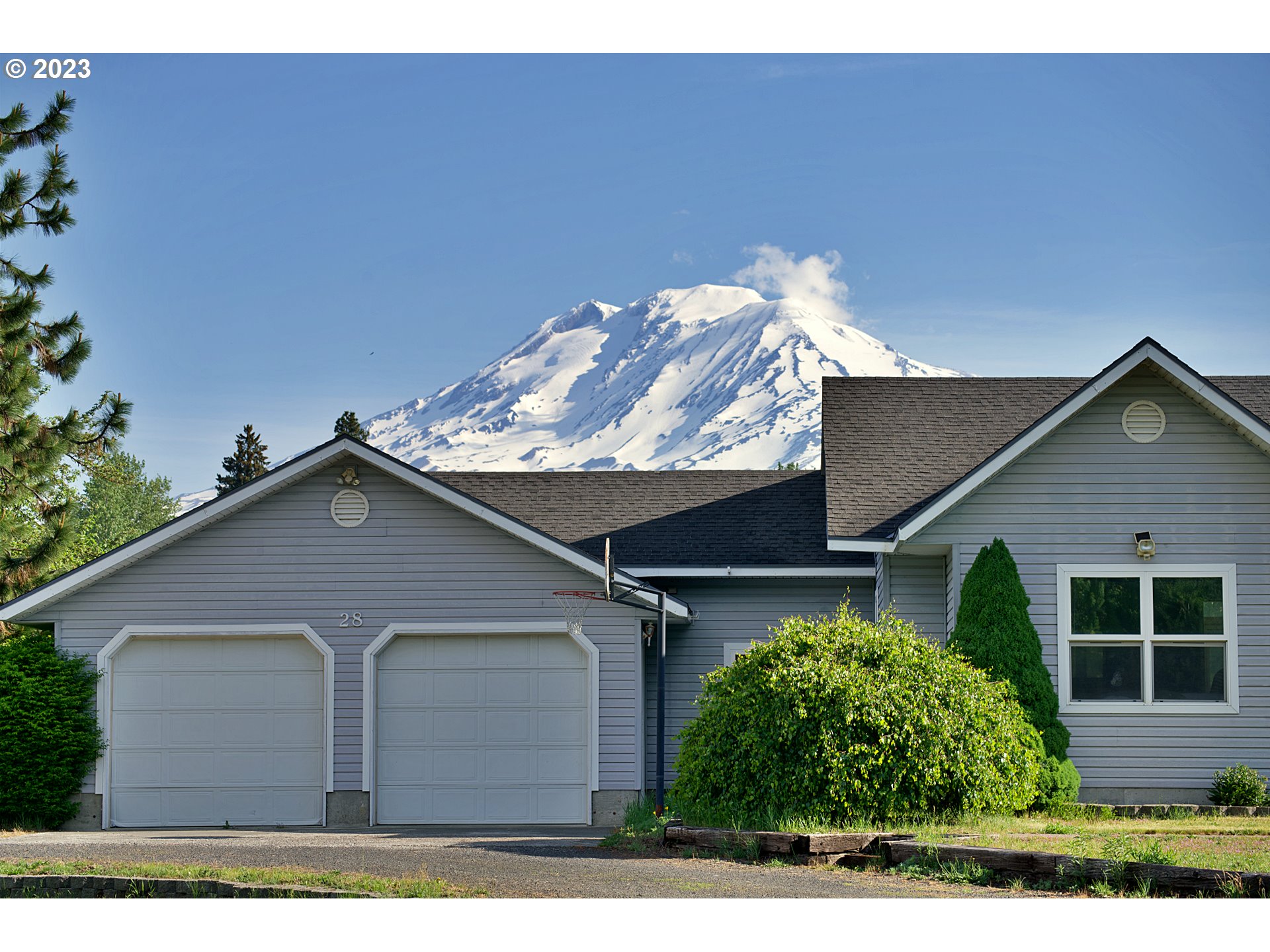 Gray house with two garage doors and a basketball hoop, backed by snow-covered Mount Adams.