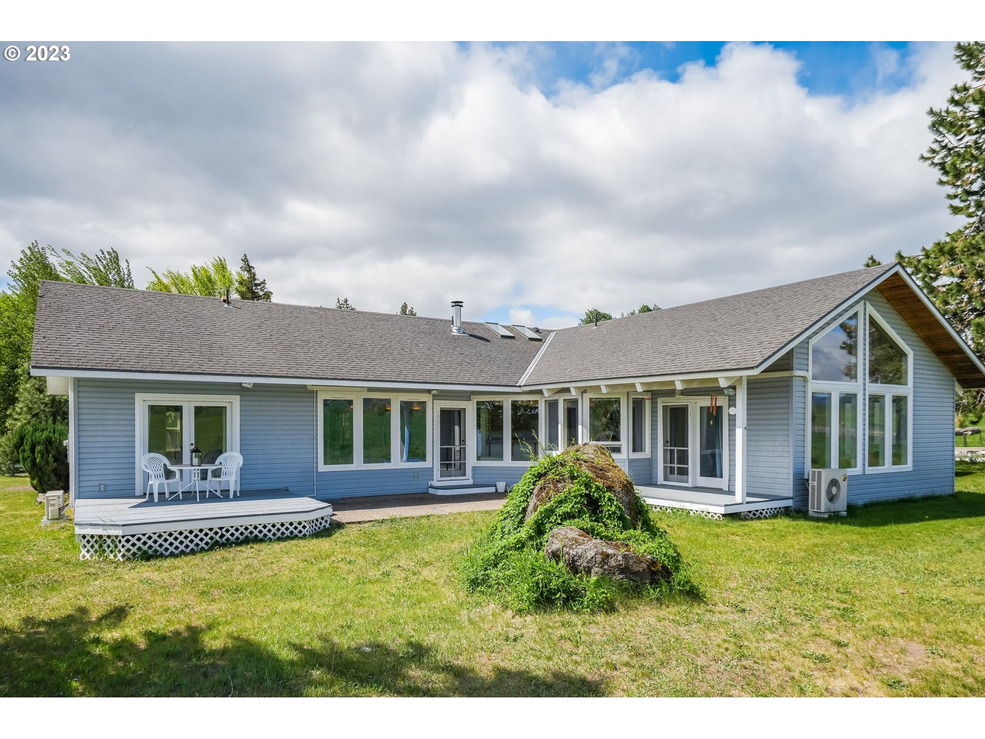 Blue-gray home with tall gabled windows, a small deck, and a grassy yard.