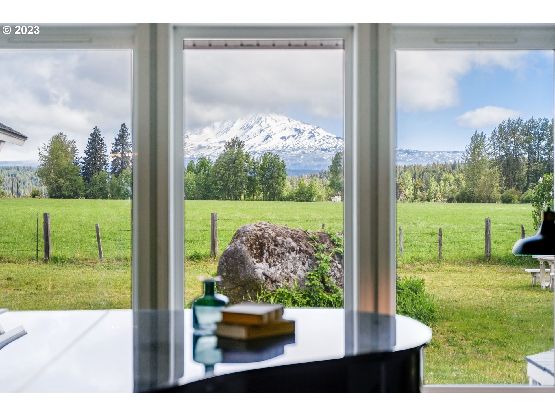 Snow-covered Mount Adams framed by windows above a green pasture and fenced field.