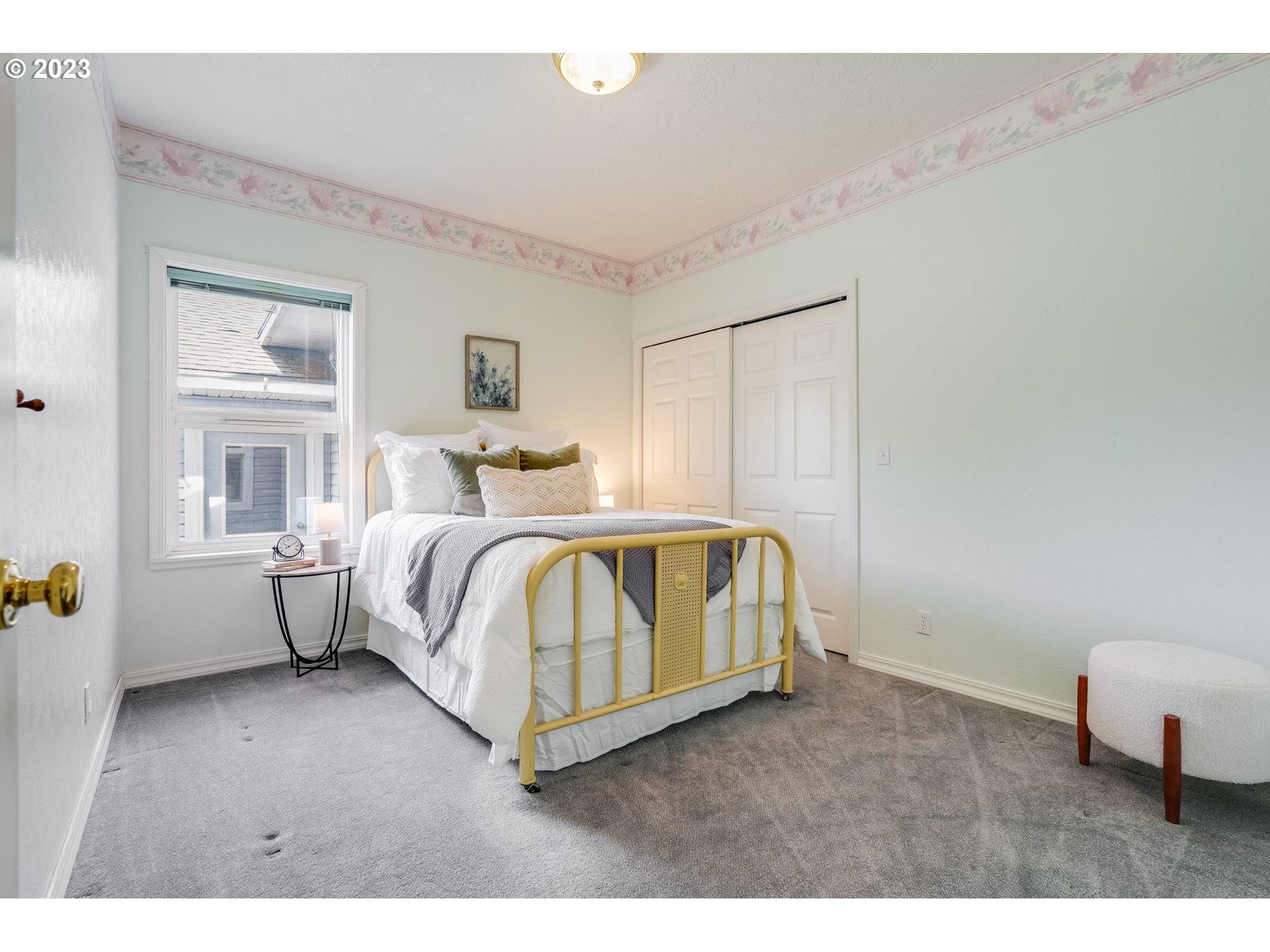 Furnished bedroom with a yellow metal bed frame, gray carpet, and floral wallpaper border.