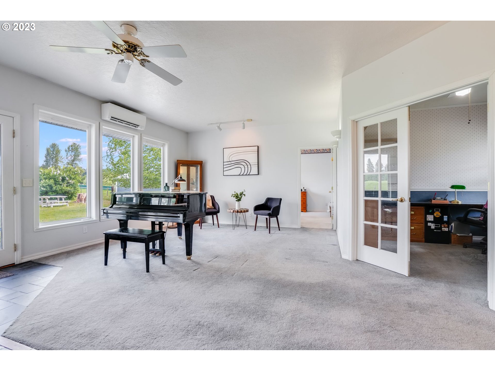 Living room with a black grand piano beside large windows overlooking a green lawn.