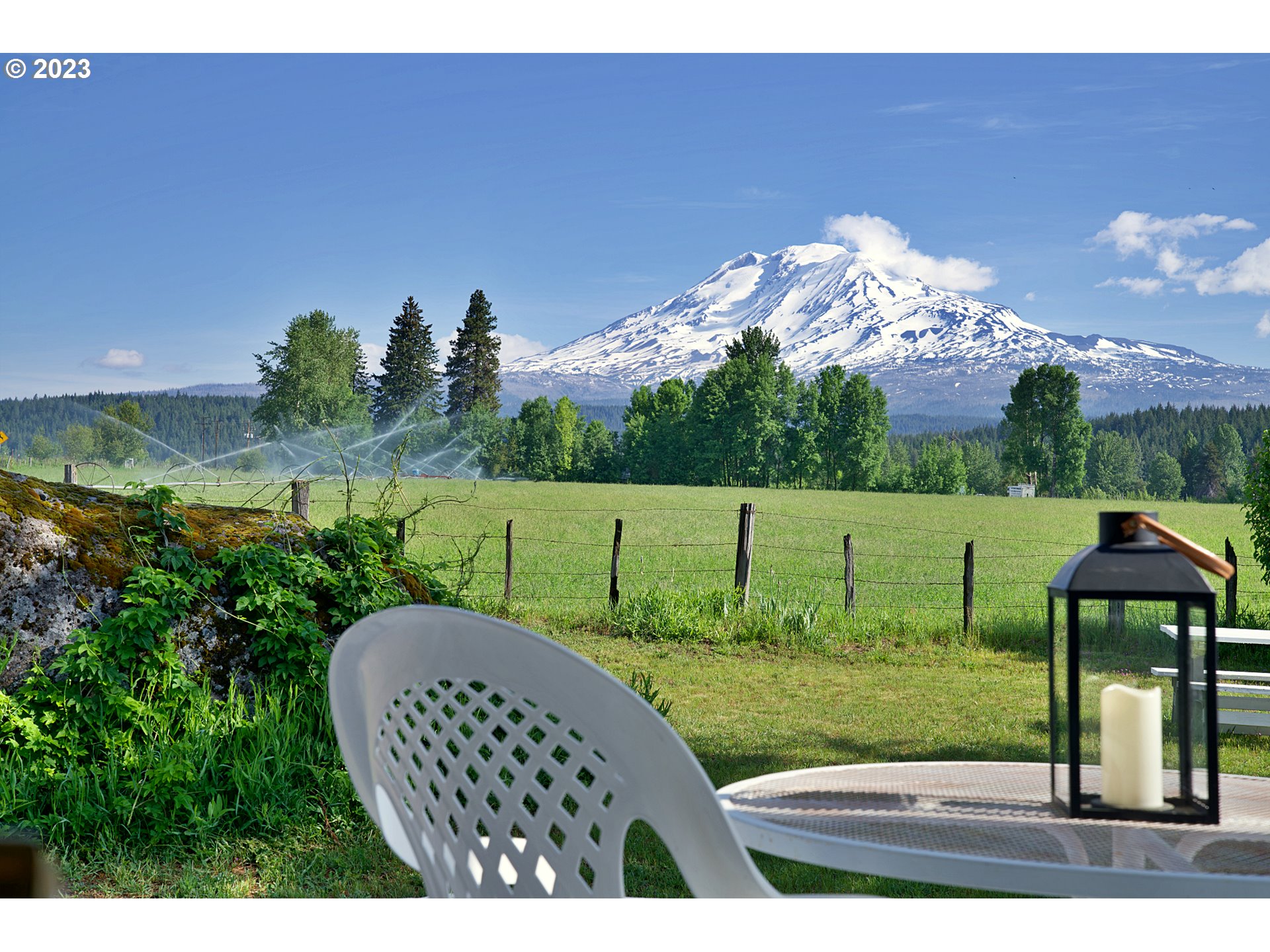 Patio seating overlooks a green field and snow-covered Mount Adams.