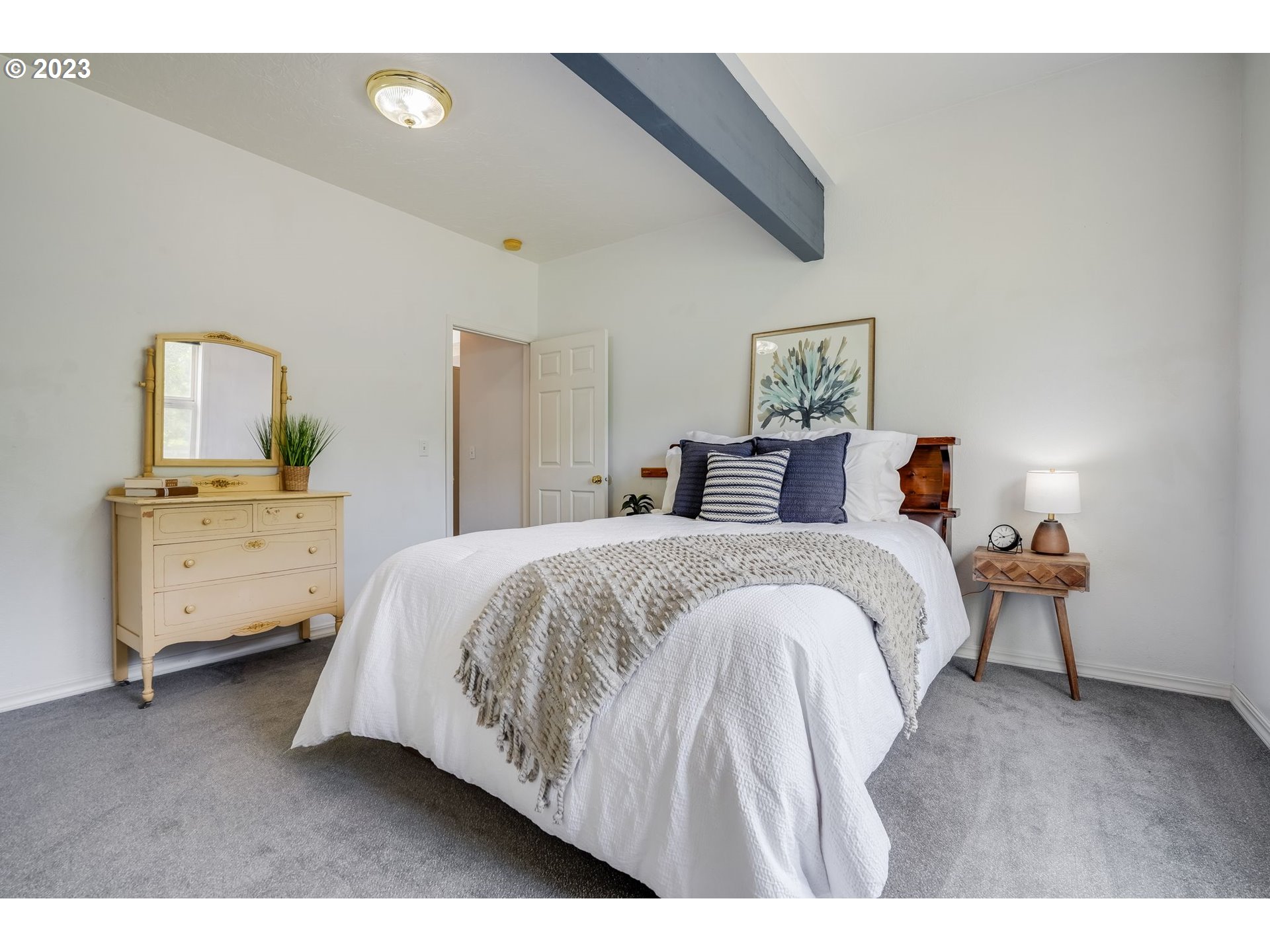 Staged bedroom with a white bed, navy pillows, gray throw, and pale yellow dresser.