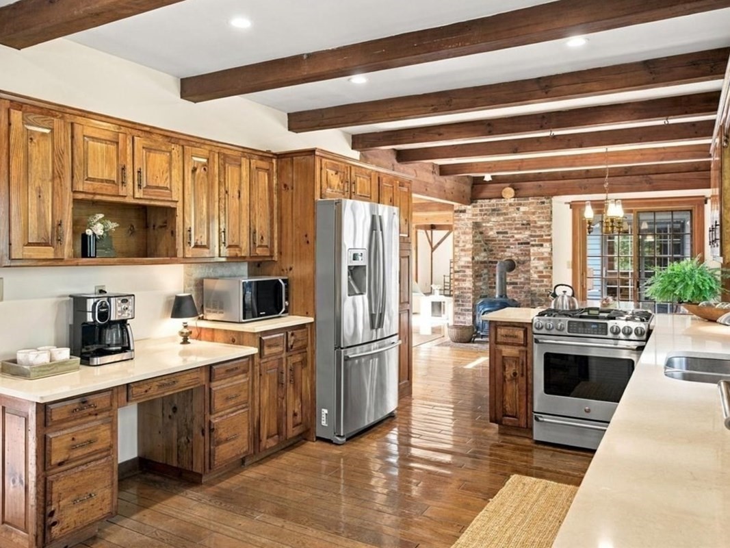 Rustic kitchen with wood cabinets, exposed beams, stainless steel appliances, and a brick wall.