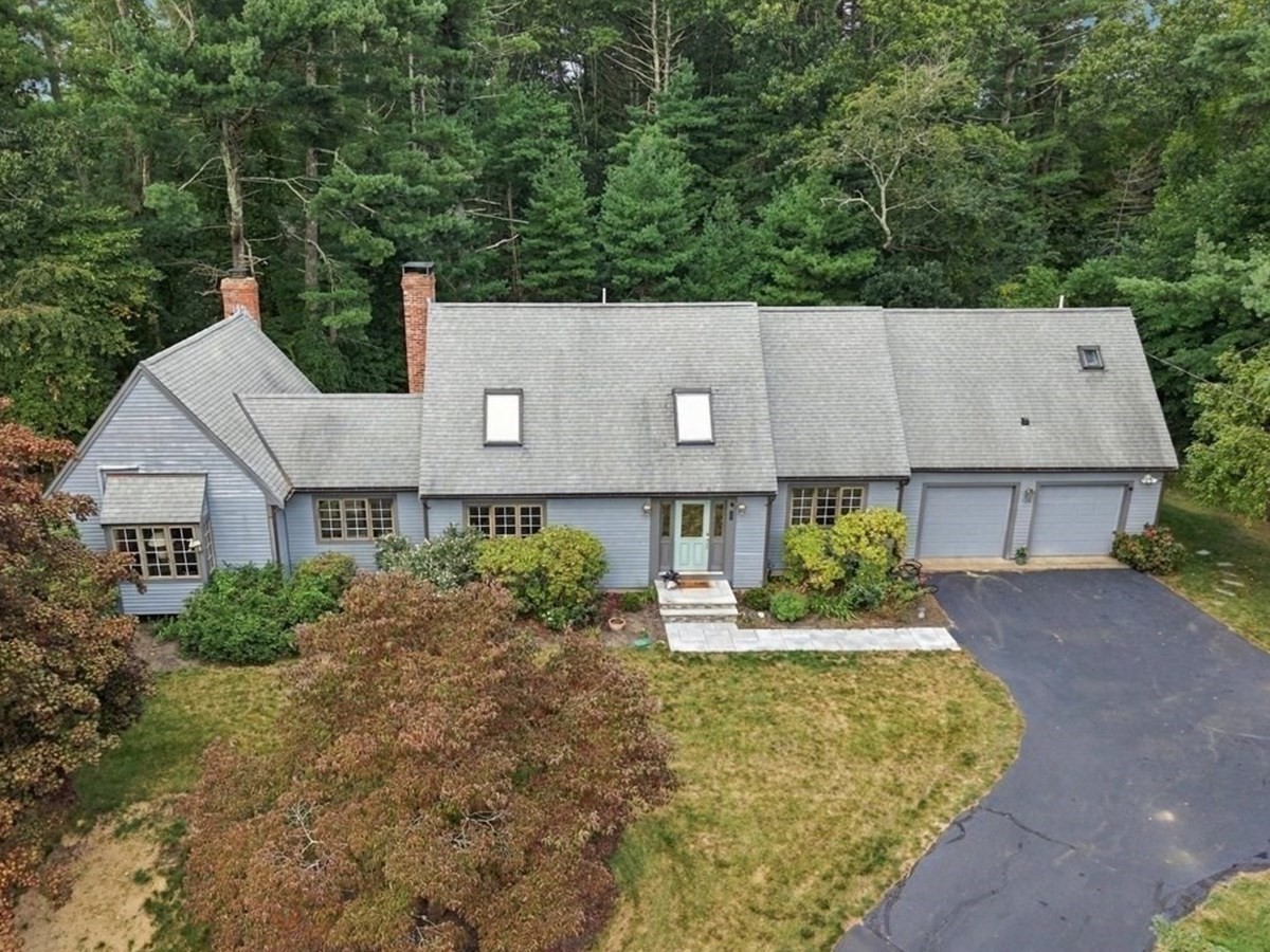 Gray-blue house with two brick chimneys, a two-car garage, and a curved driveway, viewed from above.
