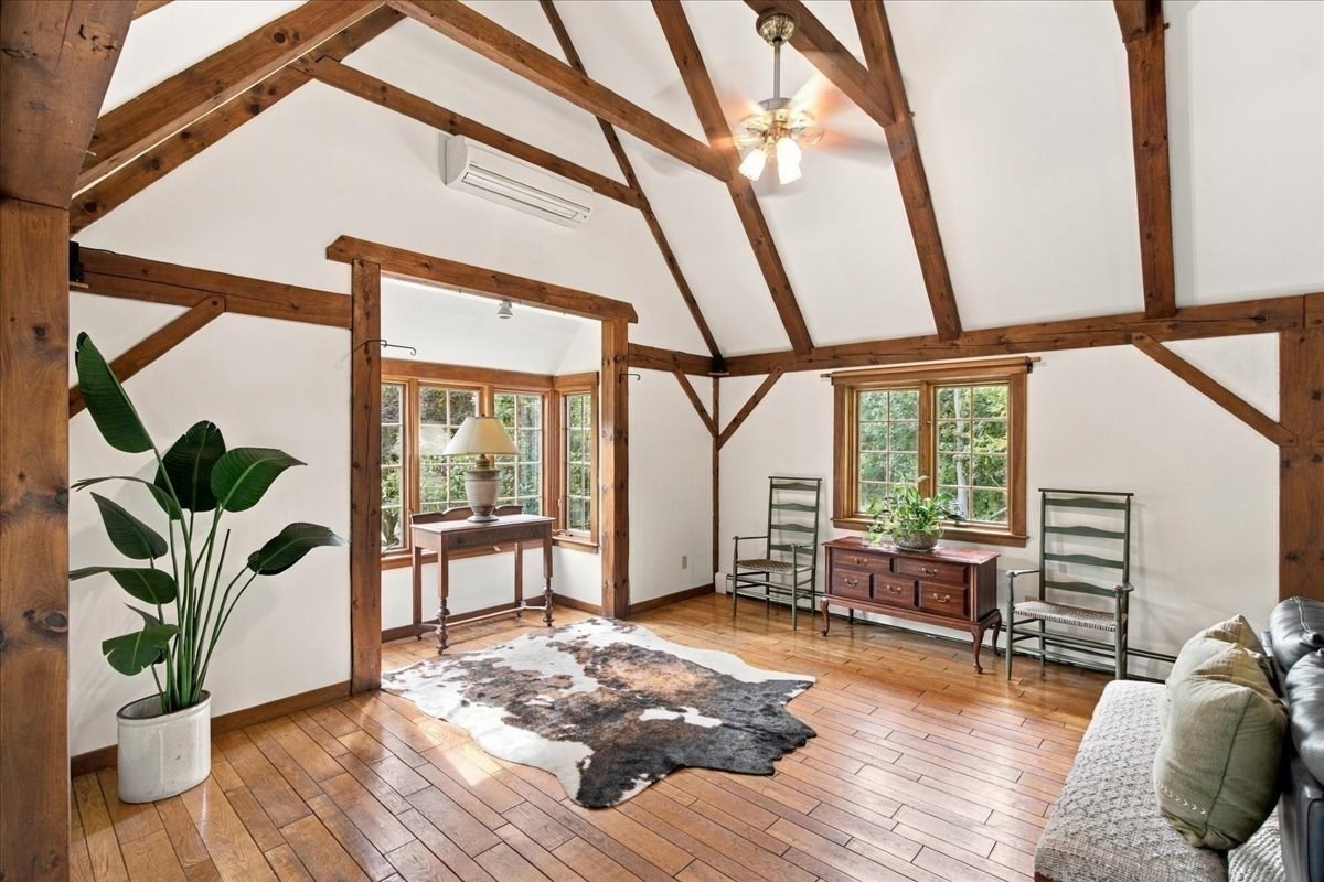 Vaulted timber-beam room with wood floors, tall windows, a potted plant, and a cowhide rug.