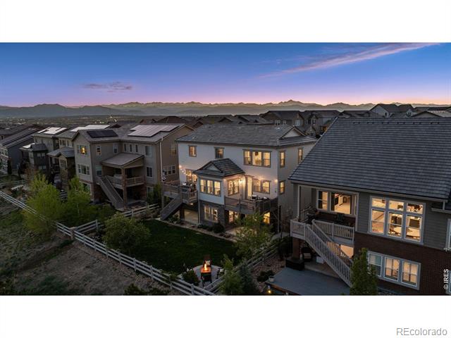Modern homes at dusk with glowing windows, fenced yards, and mountains on the horizon.