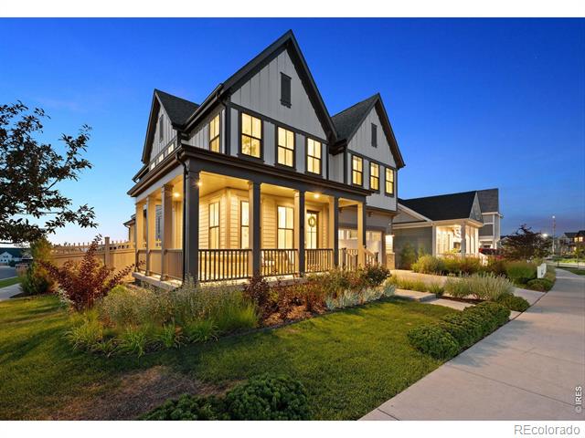 Modern two-story farmhouse with a covered porch and glowing windows at dusk.