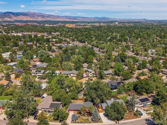 Aerial view of a leafy Boulder neighborhood with the Rocky Mountains beyond.