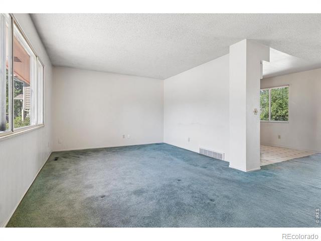 Empty living room with blue-gray carpet, large windows, and an opening to a tiled room.