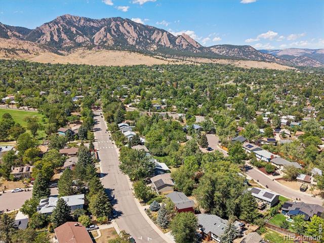 Aerial view of a leafy Boulder neighborhood with the Flatirons rising behind it.