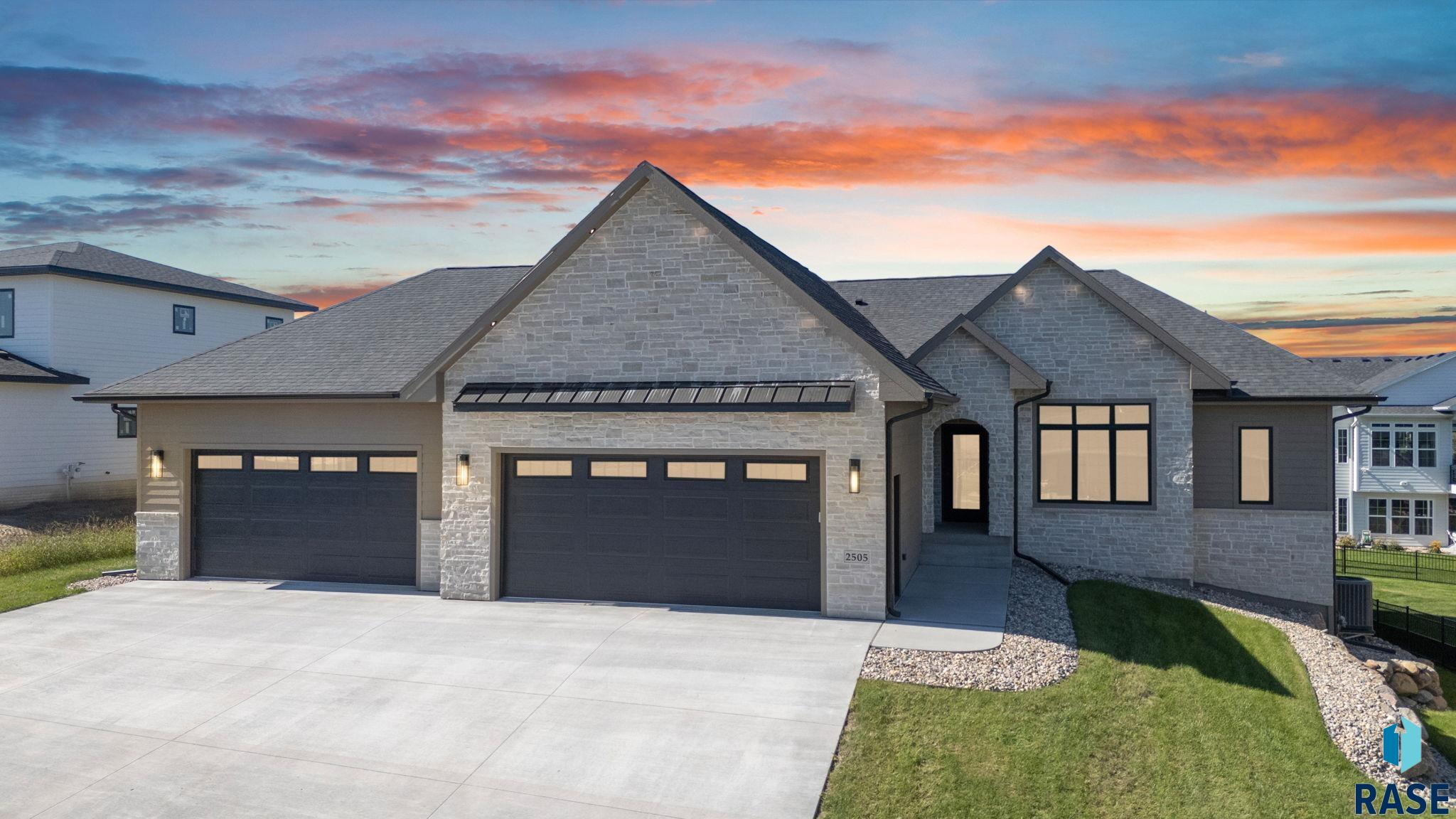 Modern gray stone home with two garages beneath a vivid sunset sky.