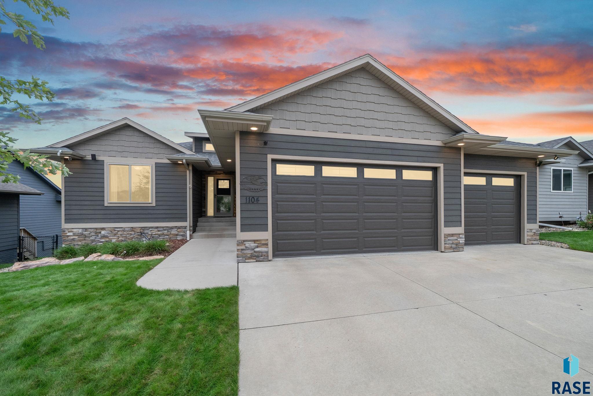 Gray house with stone accents, two garage doors, and a wide driveway at sunset.