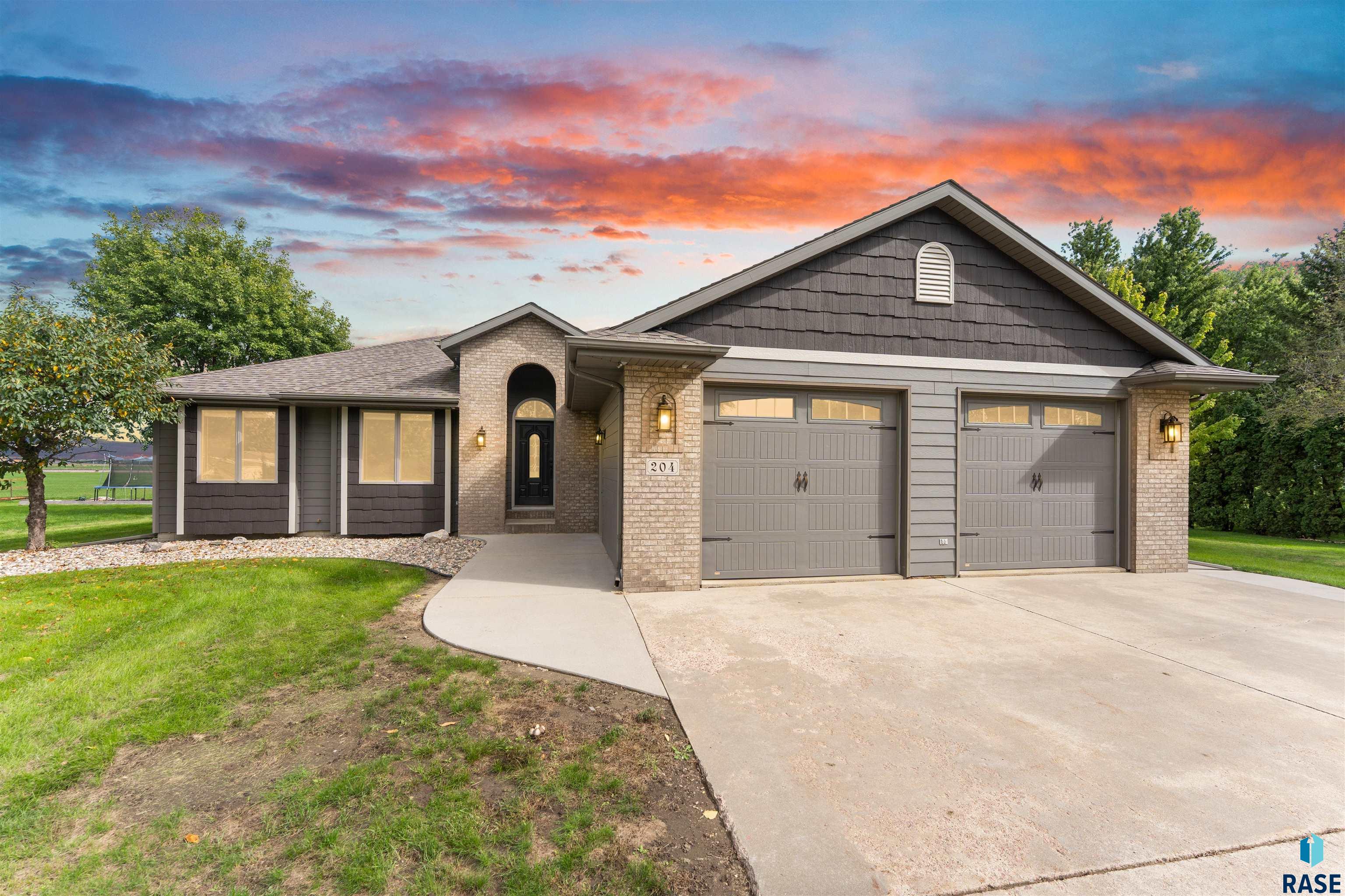 Gray single-story home with stone accents and two garage doors under a colorful sunset sky.