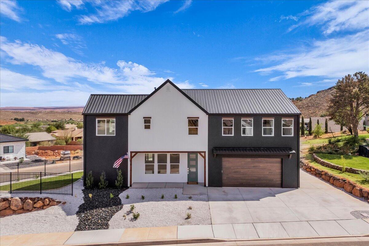 Two-story farmhouse with charcoal siding, white front gable, metal roof, and attached garage.