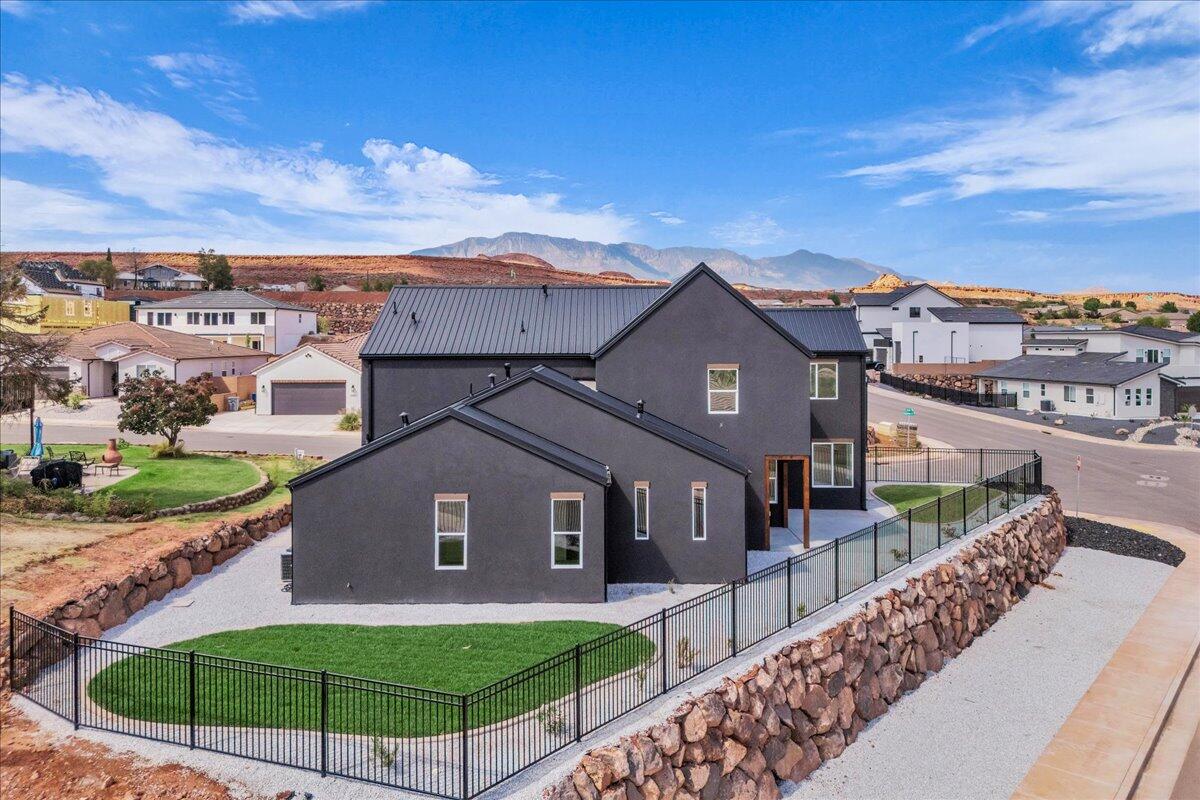 Modern charcoal-gray home with a metal roof, fenced lawn, and distant mountain views.