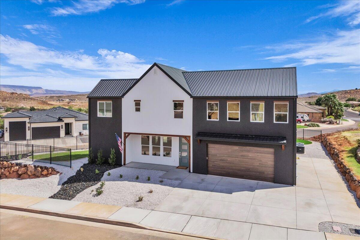 Modern two-story home with a metal roof, wood-look garage door, and desert landscaping.