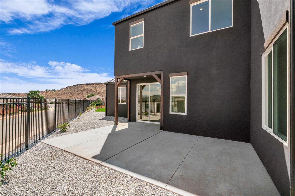 Two-story home with a covered patio, dark stucco exterior, gravel yard, and black metal fence.