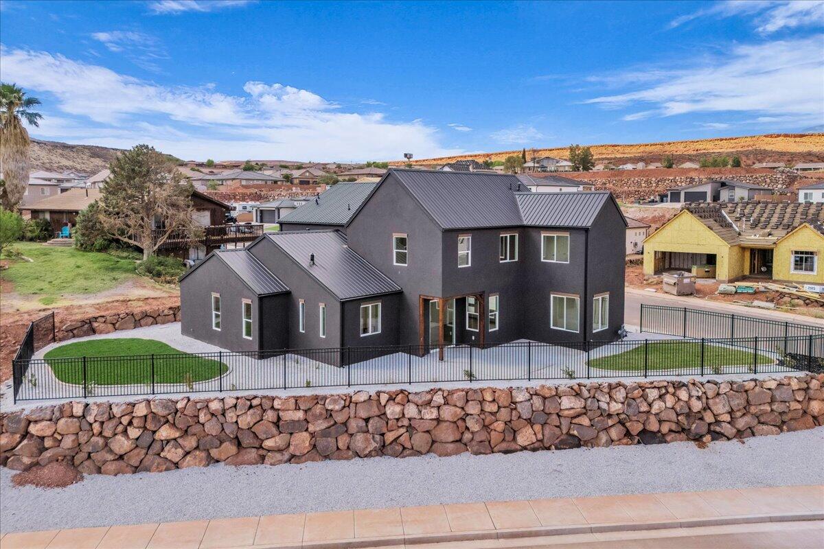 Modern dark-gray two-story home with a metal roof, fenced lawn, and stone retaining wall.
