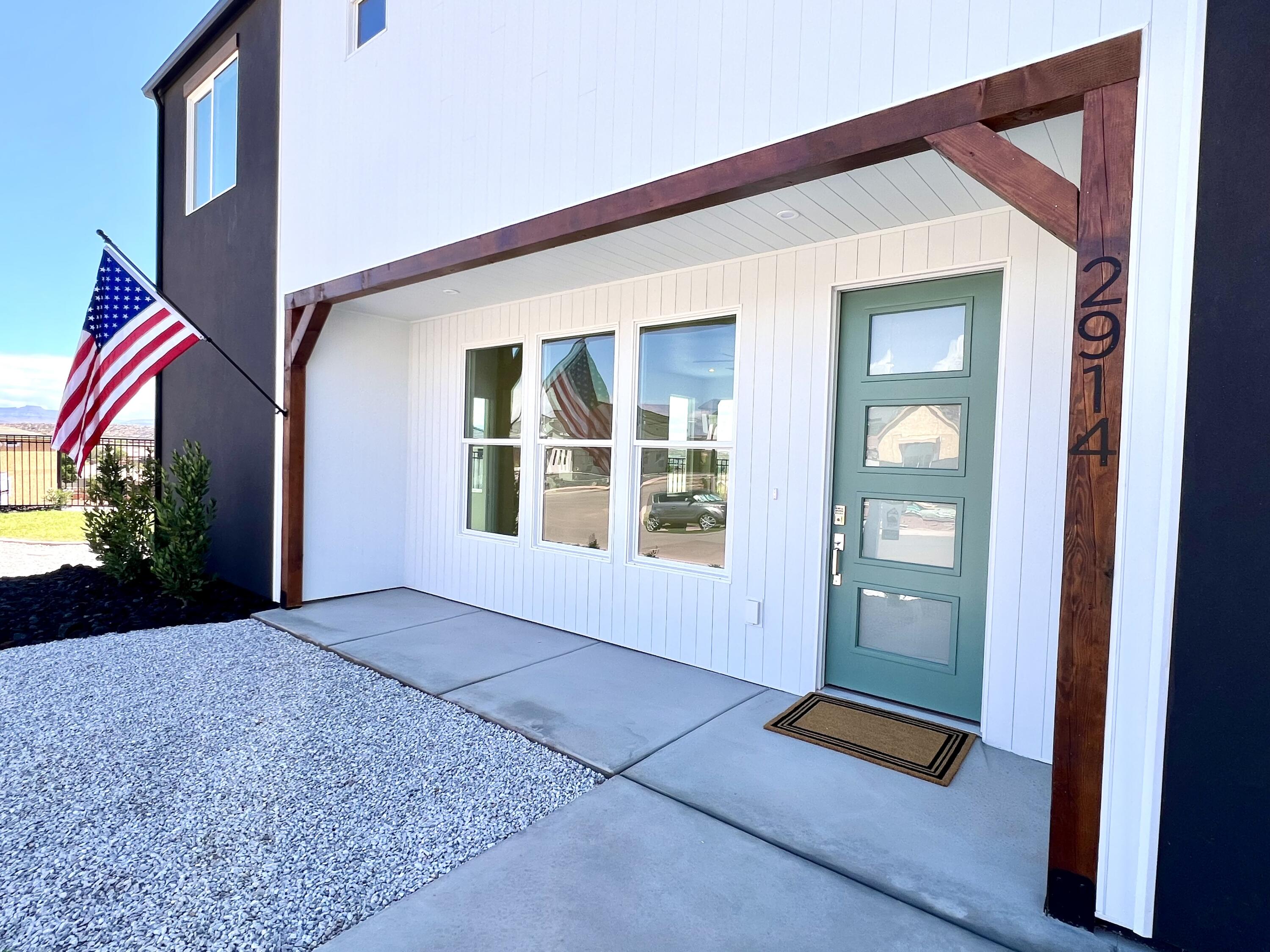 Home’s covered front entry with a teal glass-panel door, timber porch frame, and American flag.