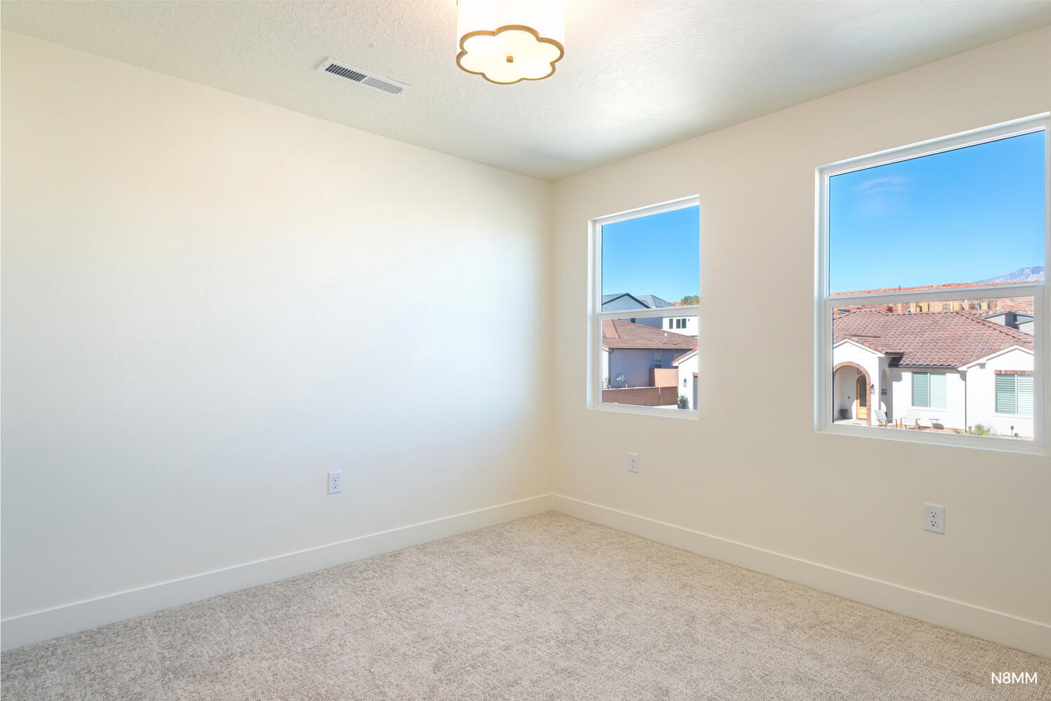 Empty carpeted bedroom with two large windows overlooking neighboring homes and distant mountains.