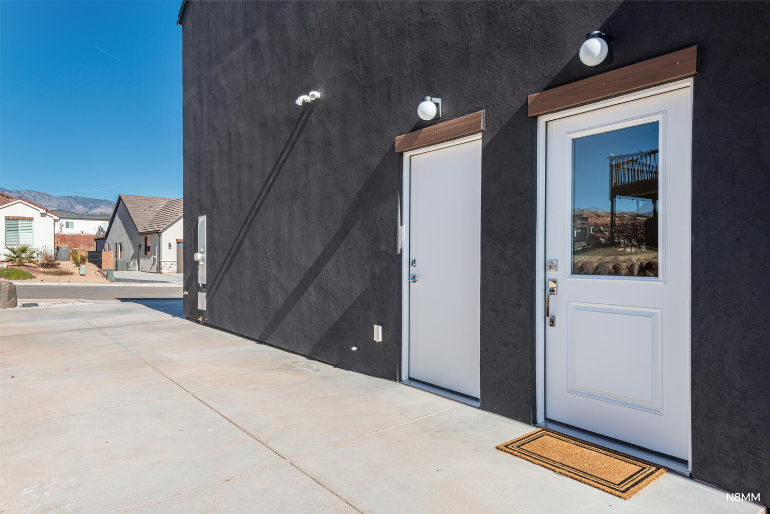 Dark stucco exterior with two white doors beside a broad concrete driveway.