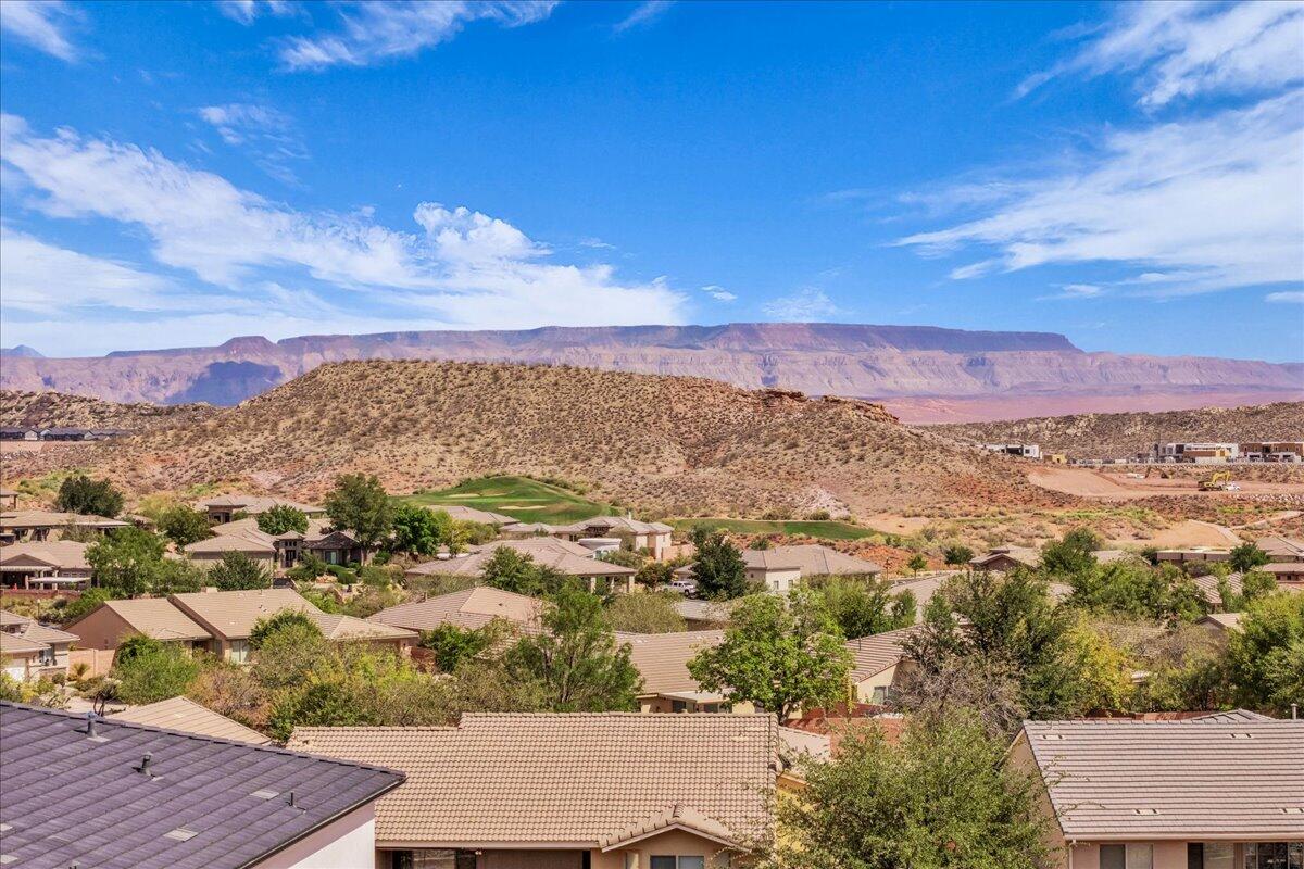 Neighborhood rooftops and a golf course below desert hills and a red rock mesa.
