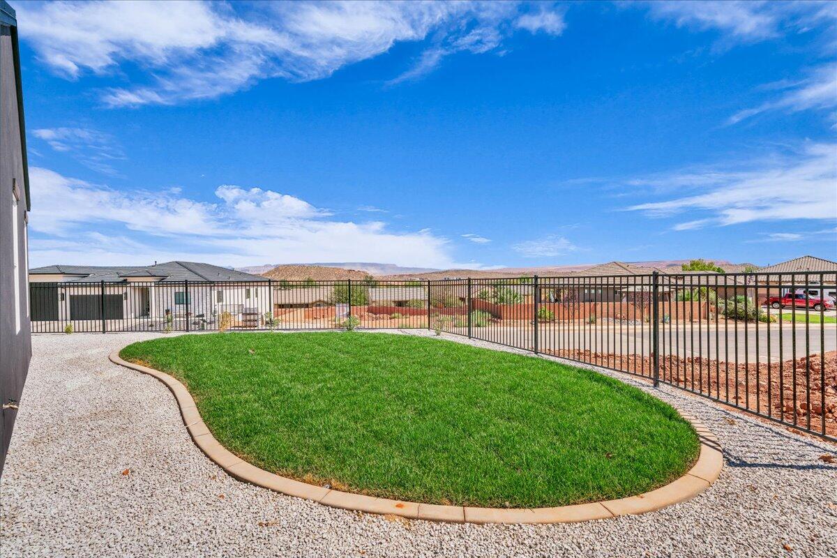 Fenced backyard with a curved green lawn, gravel border, and distant desert hills.
