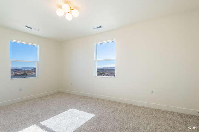 Empty carpeted room with two windows overlooking a distant landscape and sunlight on the floor.