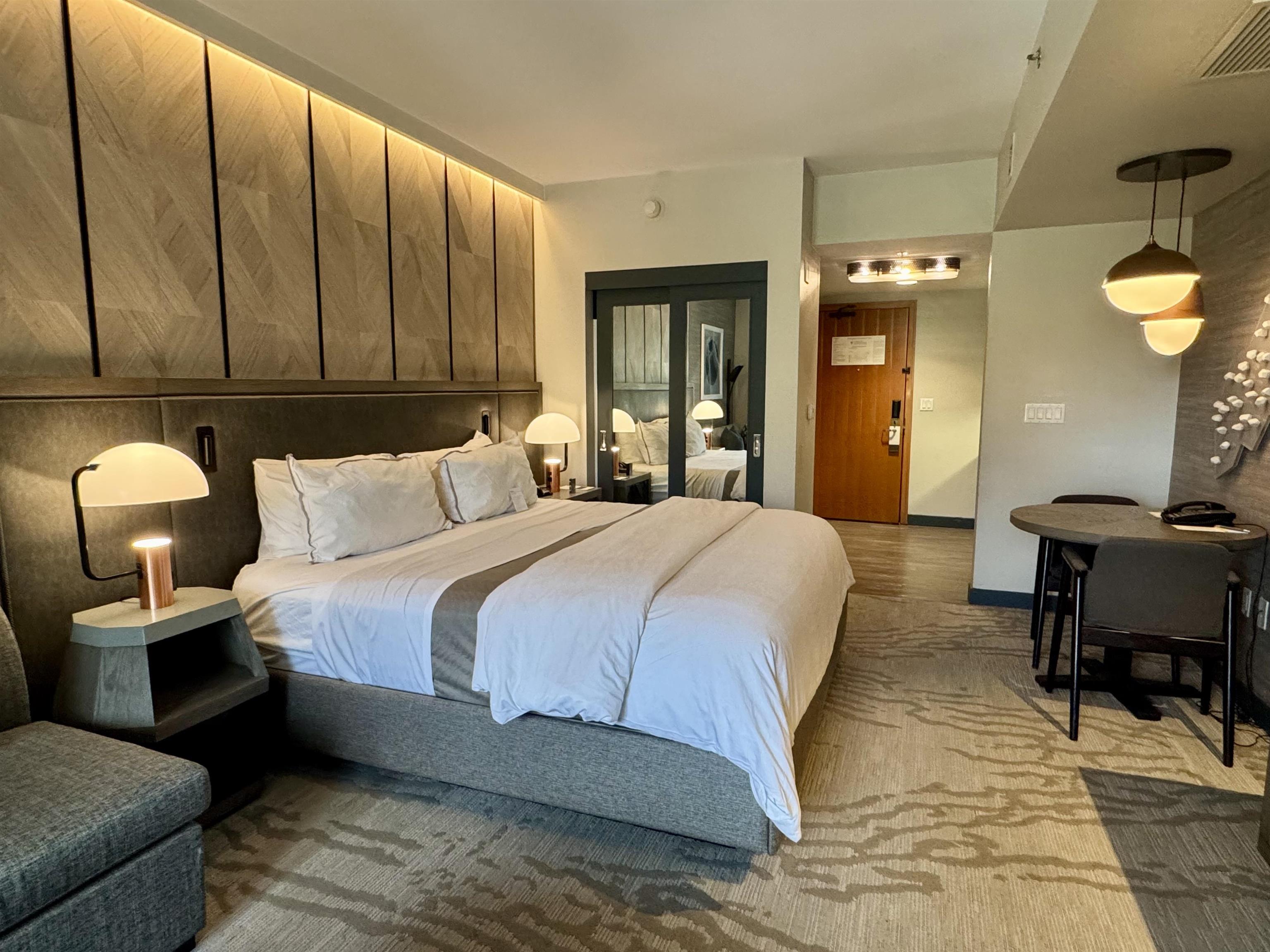 Furnished bedroom with a large bed, geometric wood wall panels, and a small dining table.