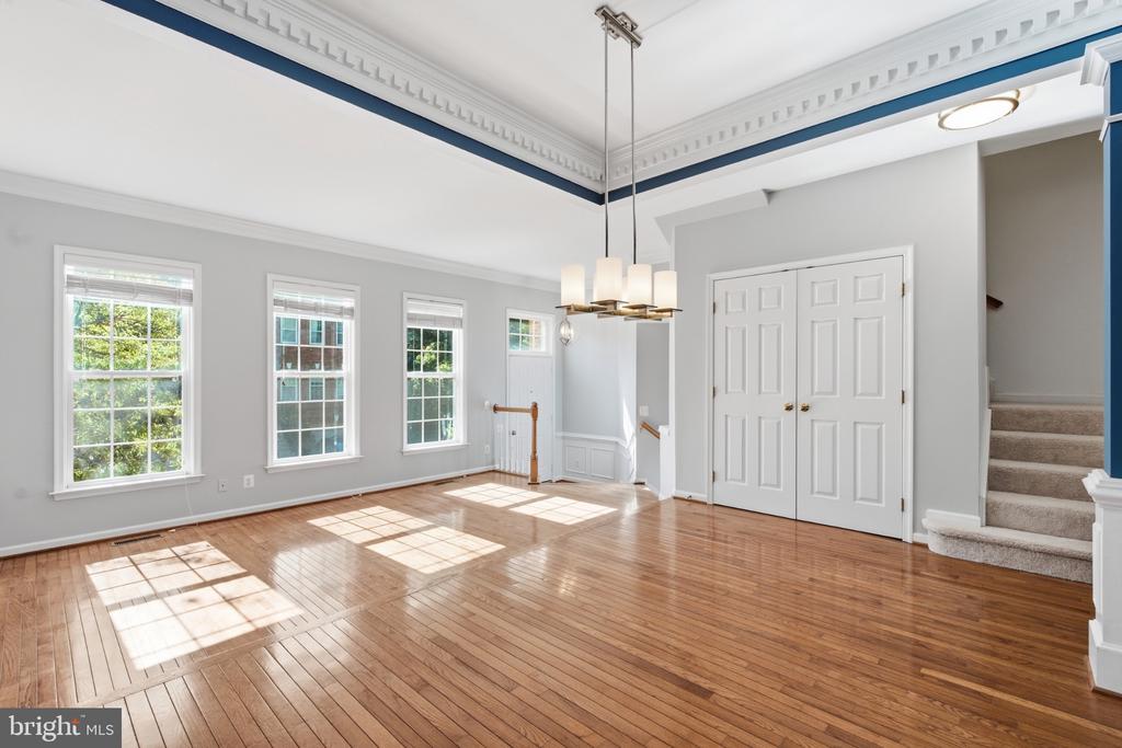 Vacant living room with polished hardwood floors, three windows, a chandelier, and stairs.