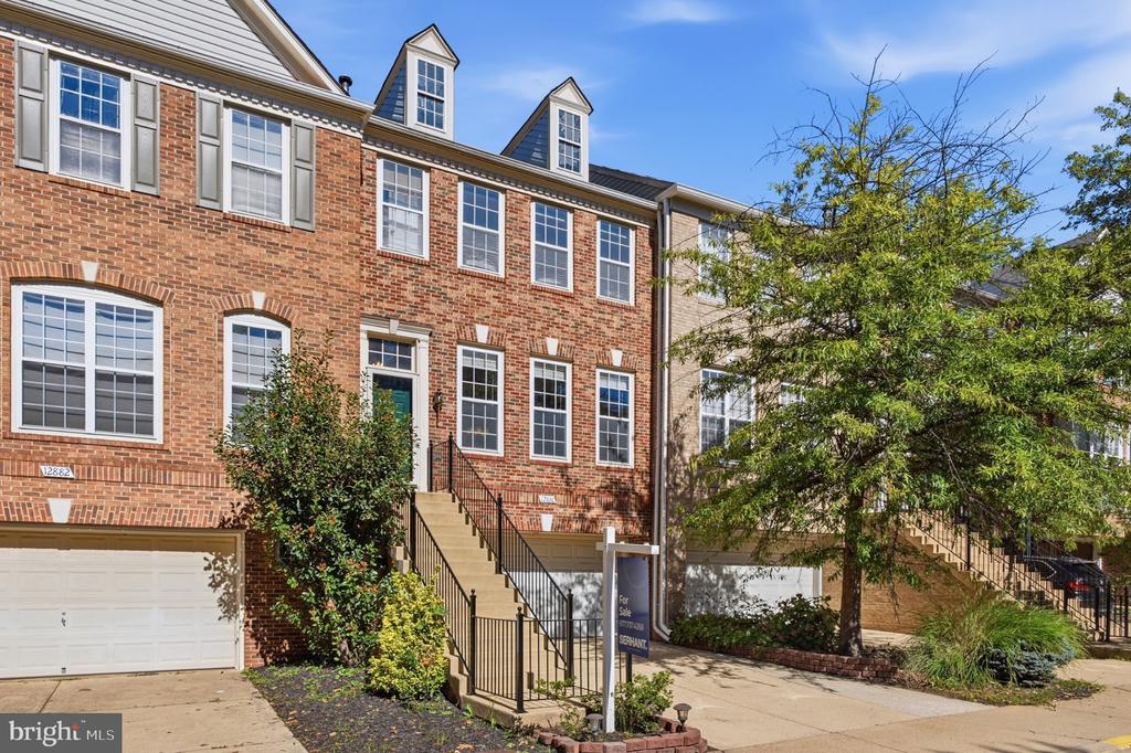 Brick townhome exterior with front steps, garage, and landscaped entry.