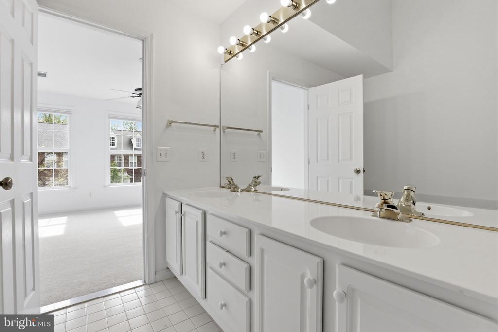 Bathroom with a long double-sink vanity and mirrored wall, opening to a bright carpeted room.