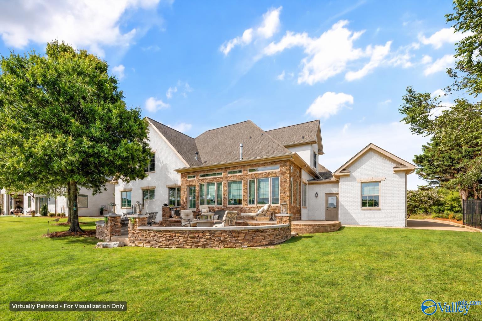 Rear of a white-brick home with a stone patio, outdoor seating, and a broad green lawn.