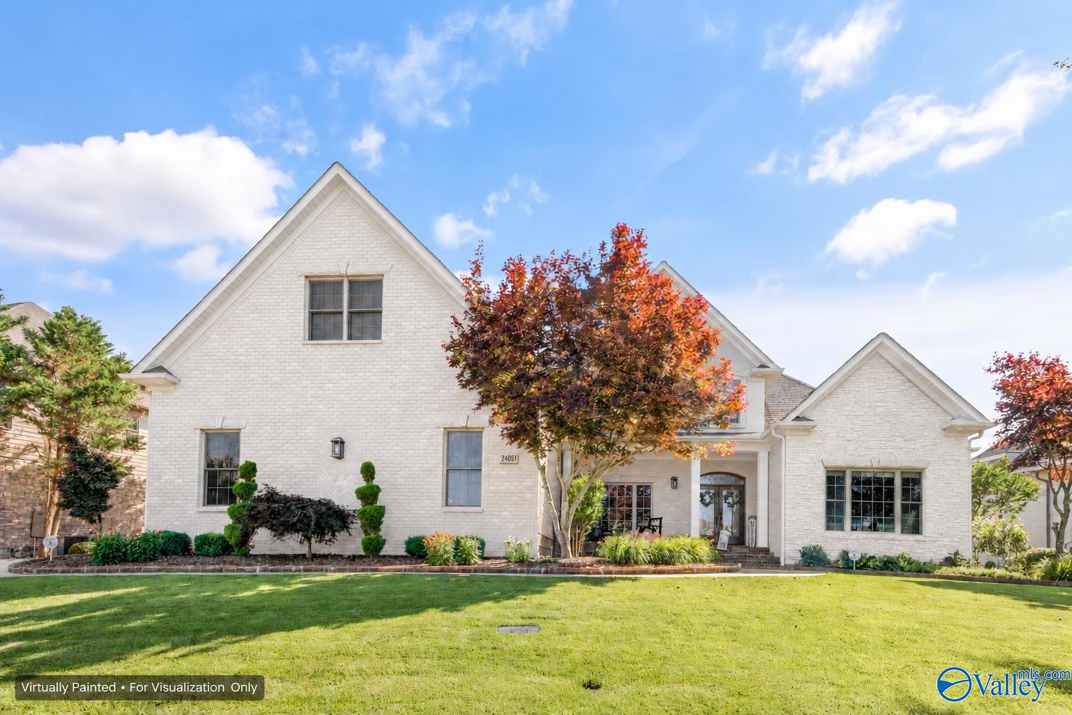 White brick house with steep gables, landscaped lawn, and colorful ornamental trees.