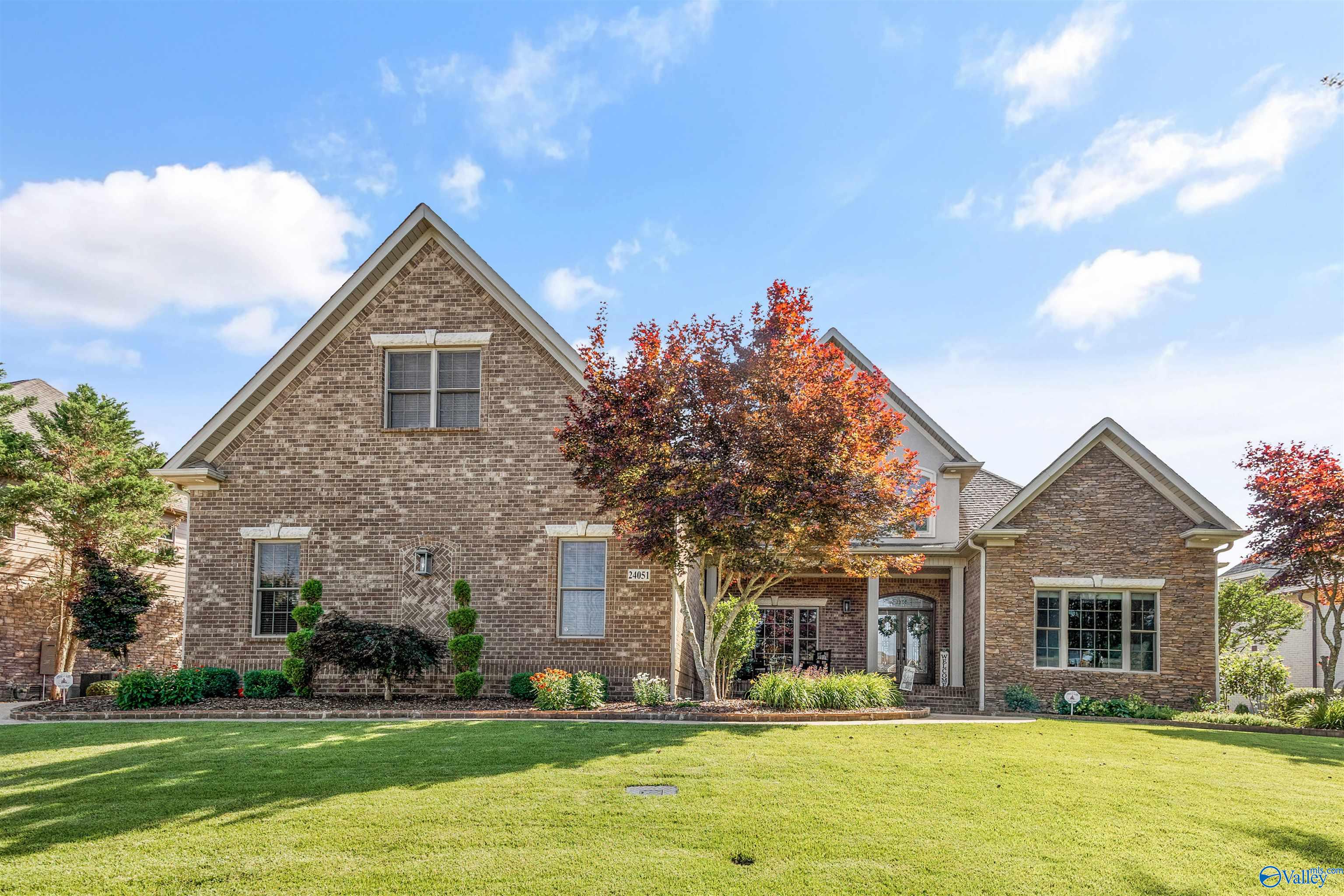 Brick-and-stone home with a broad lawn, landscaped entry, and colorful autumn trees.