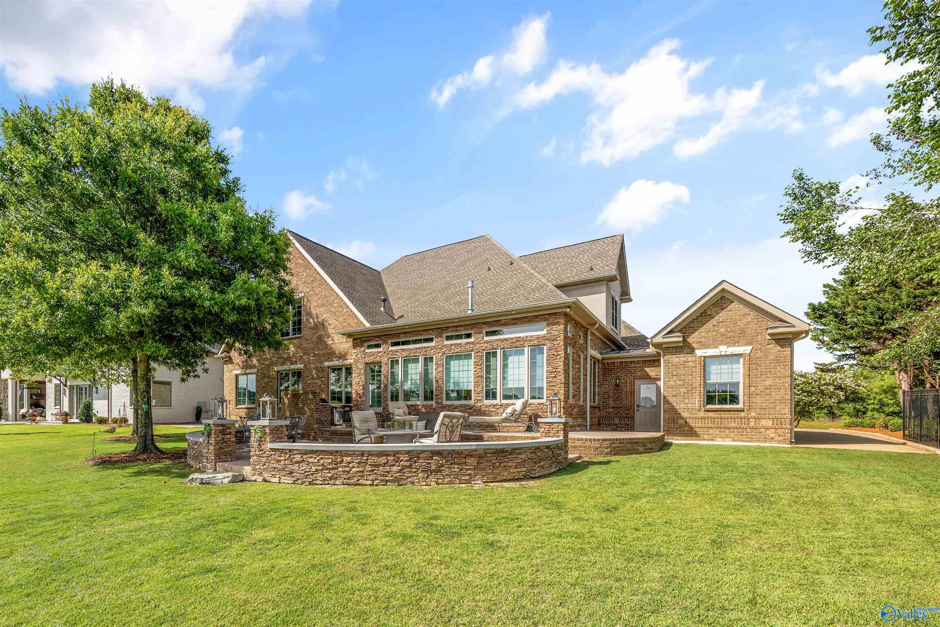 Rear exterior of brick home with a stone-edged patio, outdoor seating, and broad lawn.
