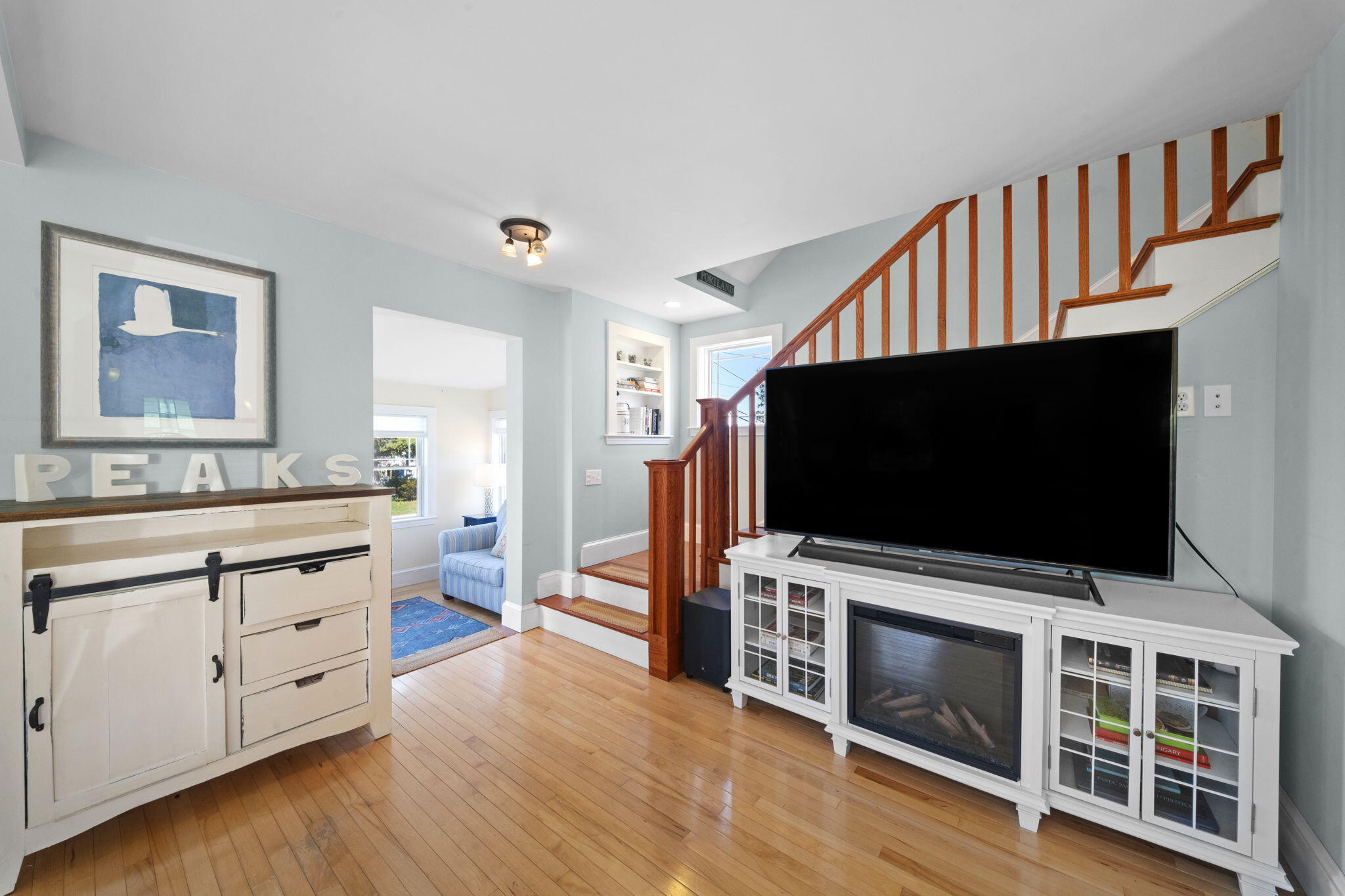 Living room with hardwood floors, a staircase, and a large TV above a fireplace.