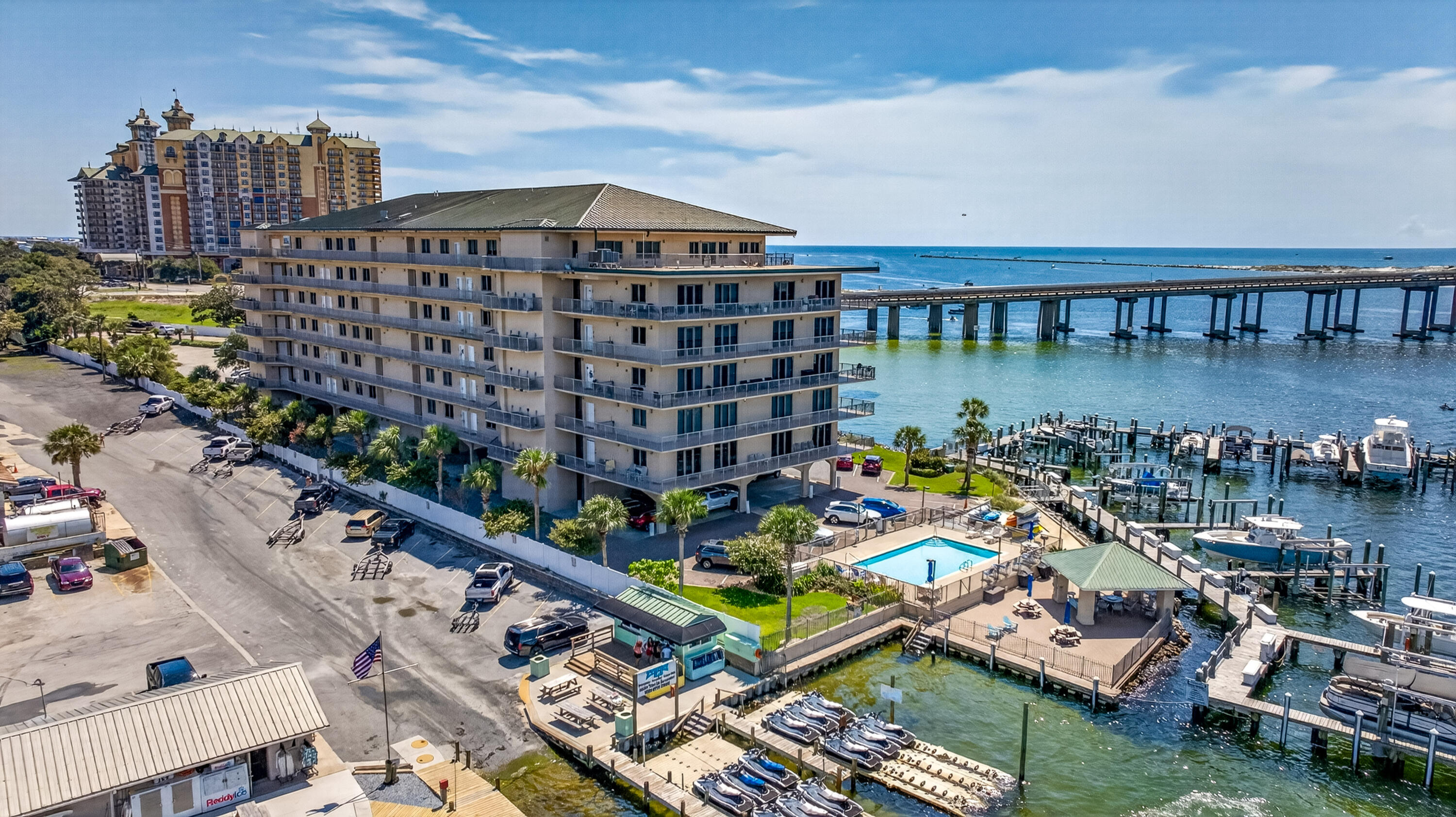 Waterfront condominium with balconies, a pool, marina docks, and boats beside a bridge.