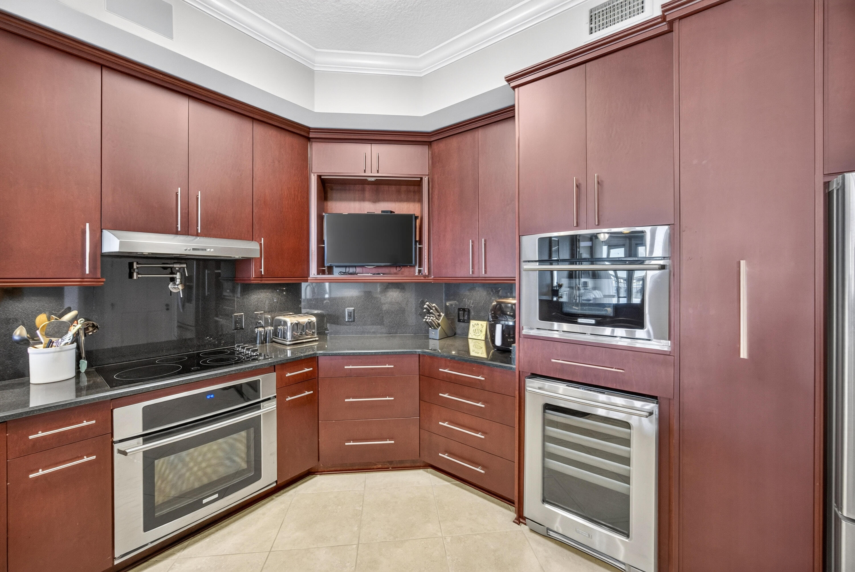 Kitchen with reddish wood cabinets, dark stone counters, stainless appliances, and a television built into the cabinetry.