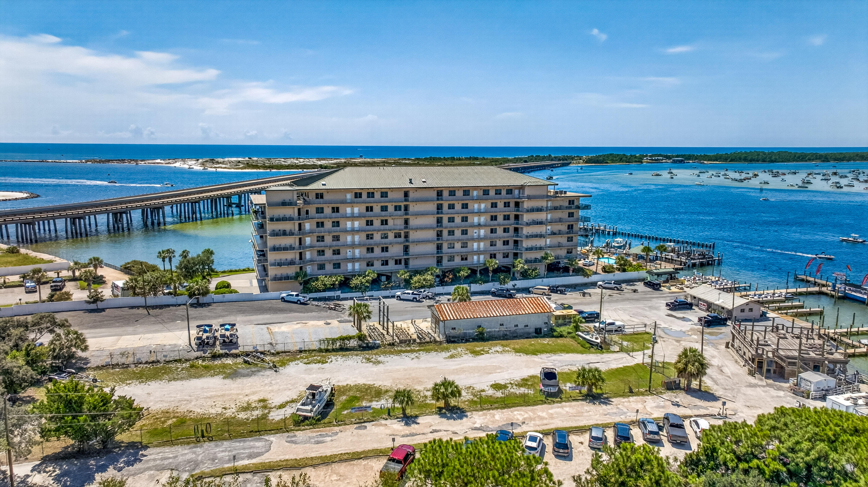 Waterfront condominium beside a bridge and marina, surrounded by bright blue water and boats.