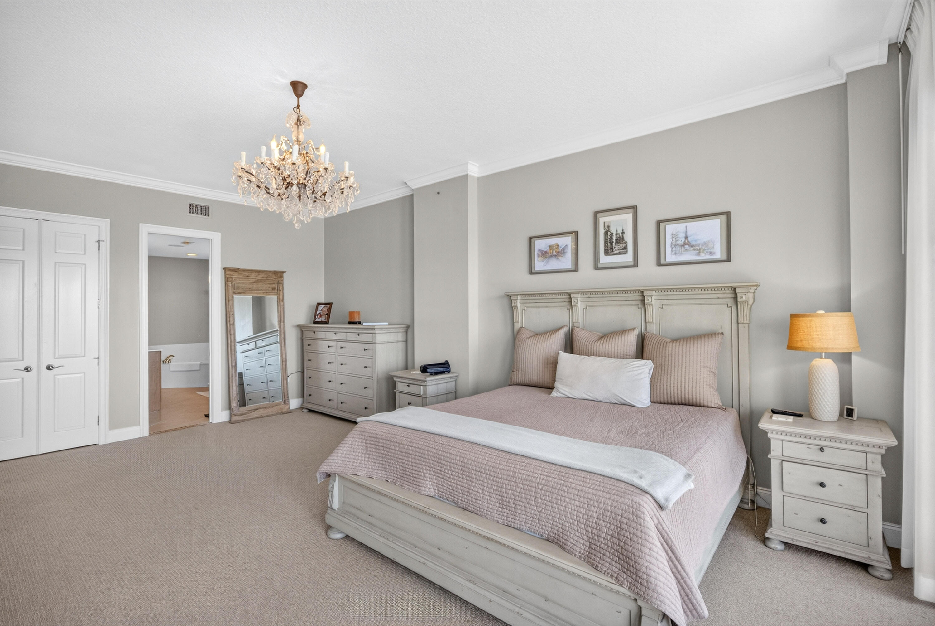 Bedroom with a large mauve-quilted bed, ornate white headboard, and crystal chandelier.
